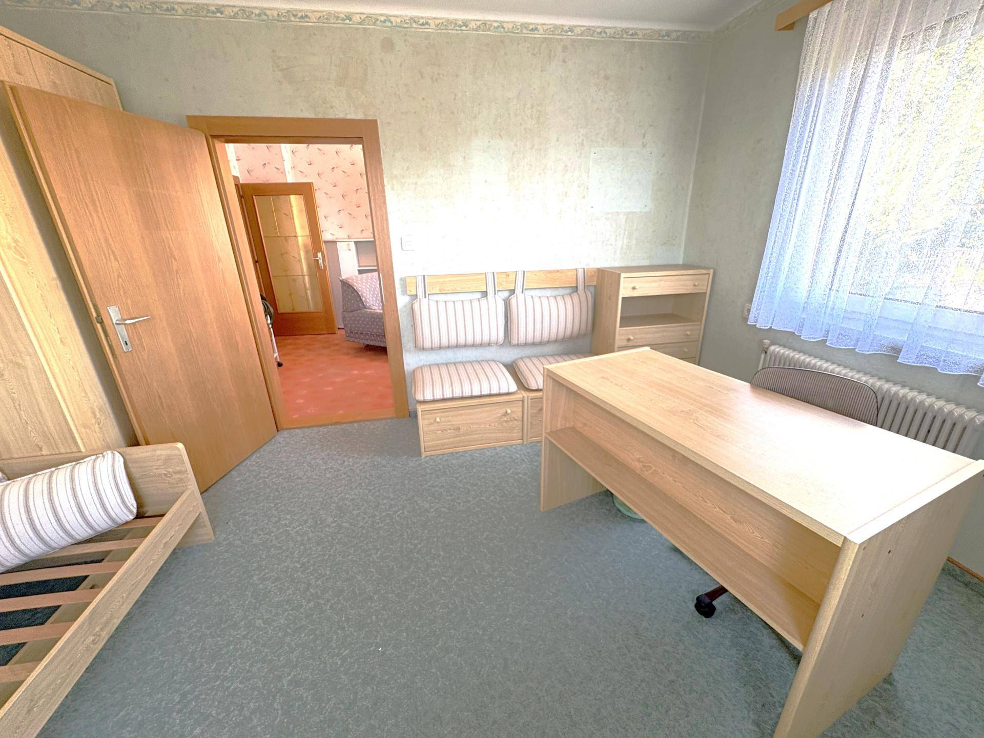 Helles Arbeitszimmer mit Schreibtisch, Stuhl und Blick in einen angrenzenden Raum.