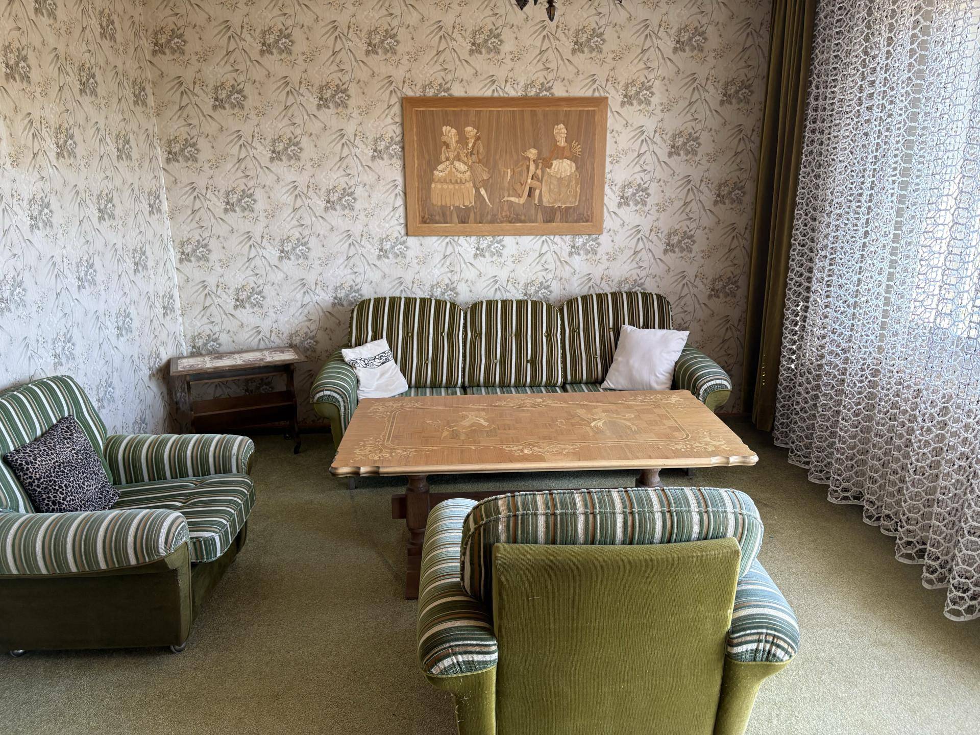 Wohnzimmer mit gestreiften Polstermöbeln, einem Holztisch und gemusterter Tapete.