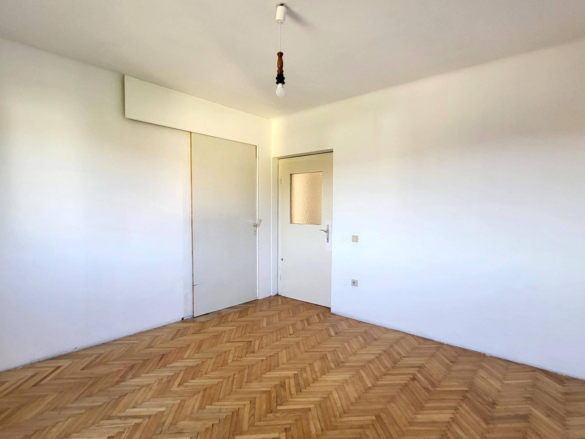 Leeres Schlafzimmer mit Parkettboden und Einbauschrank an der Wand, bietet praktischen Stauraum.