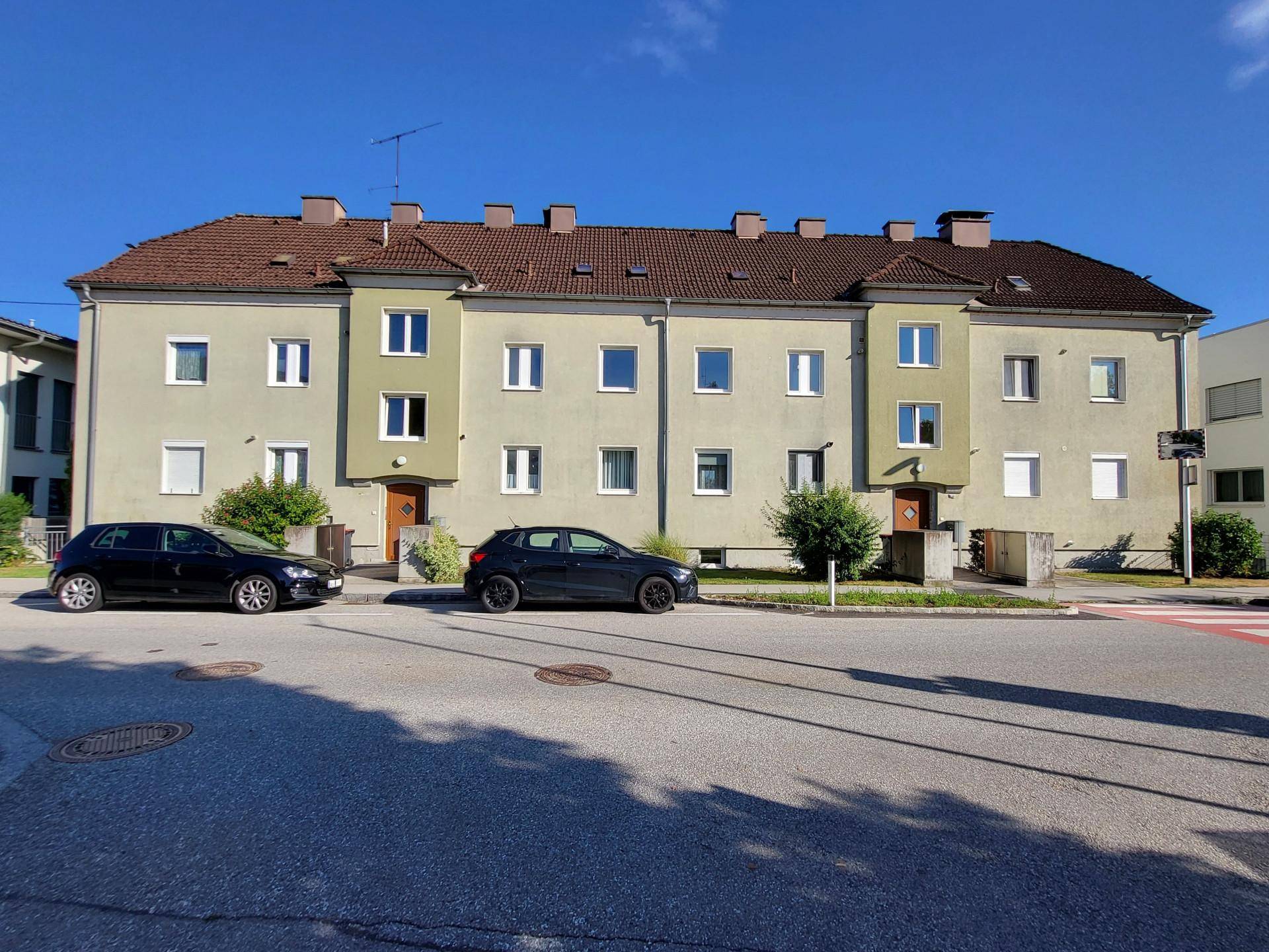 Mehrfamilienhaus mit mehreren Eingängen und geparkten Autos auf der Straße, in einer ruhigen Wohngegend.