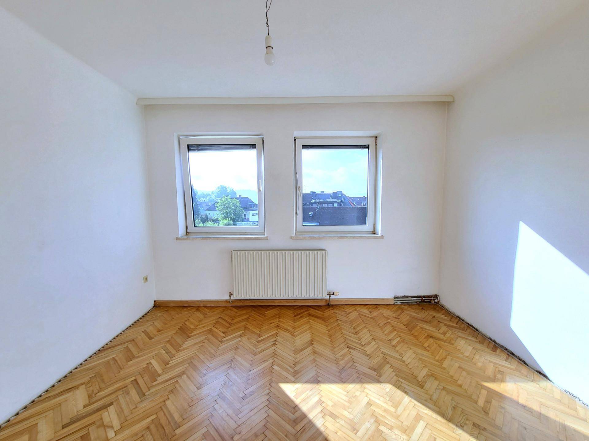 Helles Schlafzimmer mit zwei Fenstern, Heizkörpern und klassischem Parkettboden, bietet viel Gestaltungspotenzial.