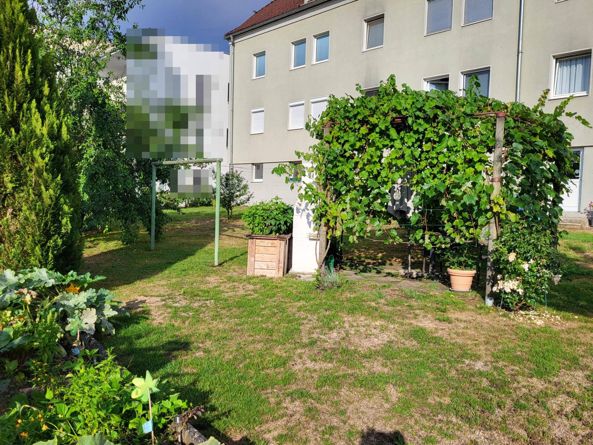 Grüner Garten mit Rasen, Pflanzen und einem Hochbeet vor dem Gebäude, ideal für Gartenliebhaber.