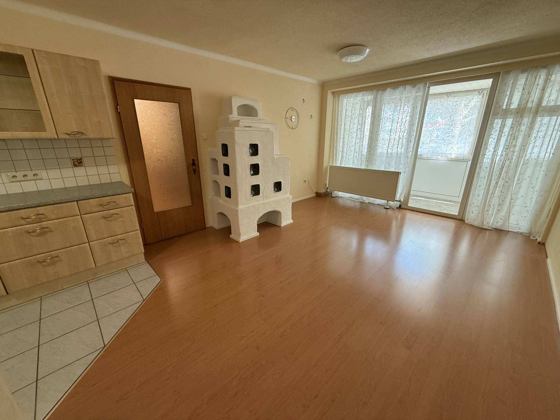 Gemütlicher Wohnbereich mit Kachelofen, Laminatboden und Zugang zu einem Balkon durch große Fenster.