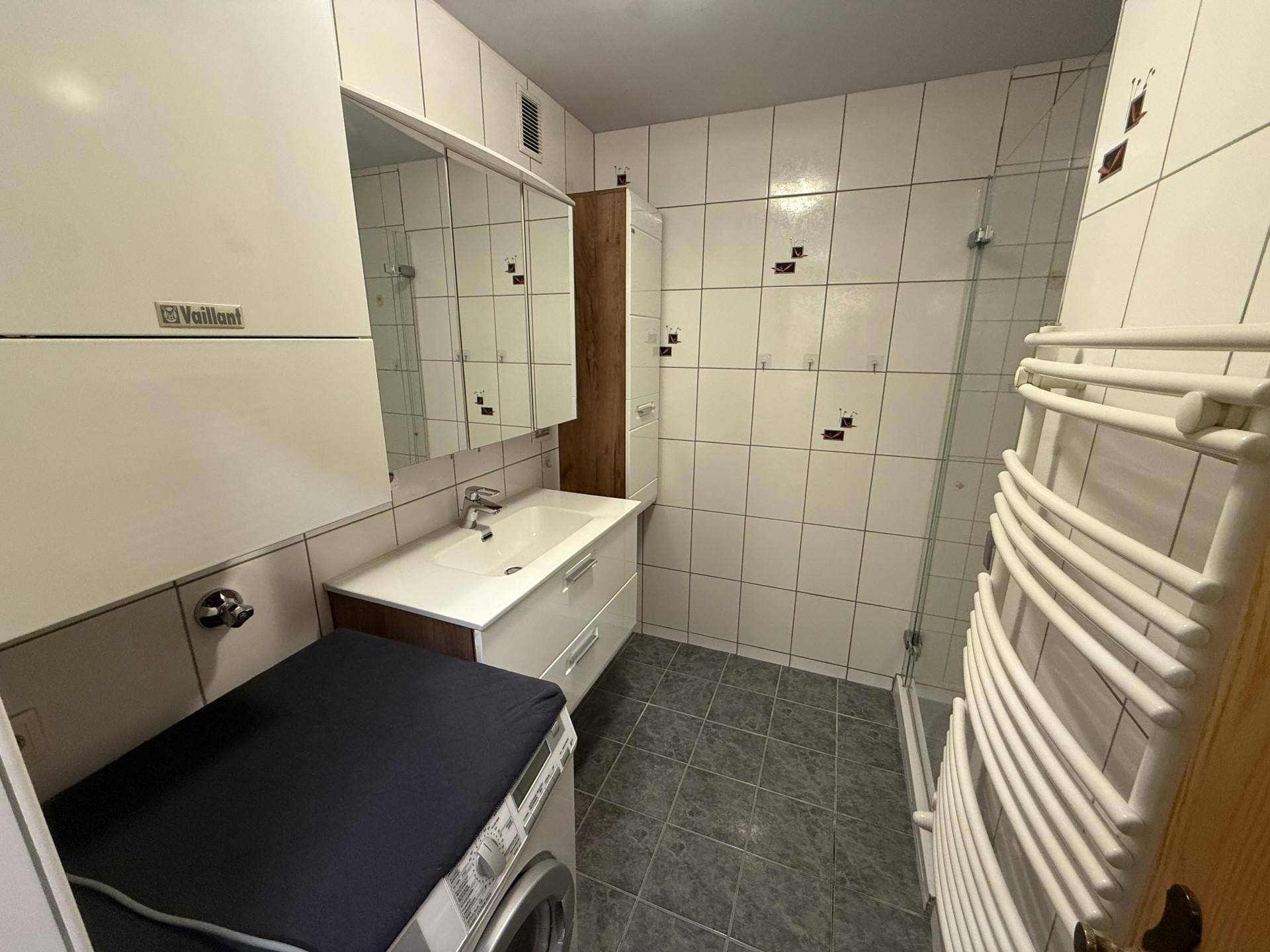 Modernes Badezimmer mit weißen Fliesen, Waschbecken, Spiegelschrank und einer Duschkabine.