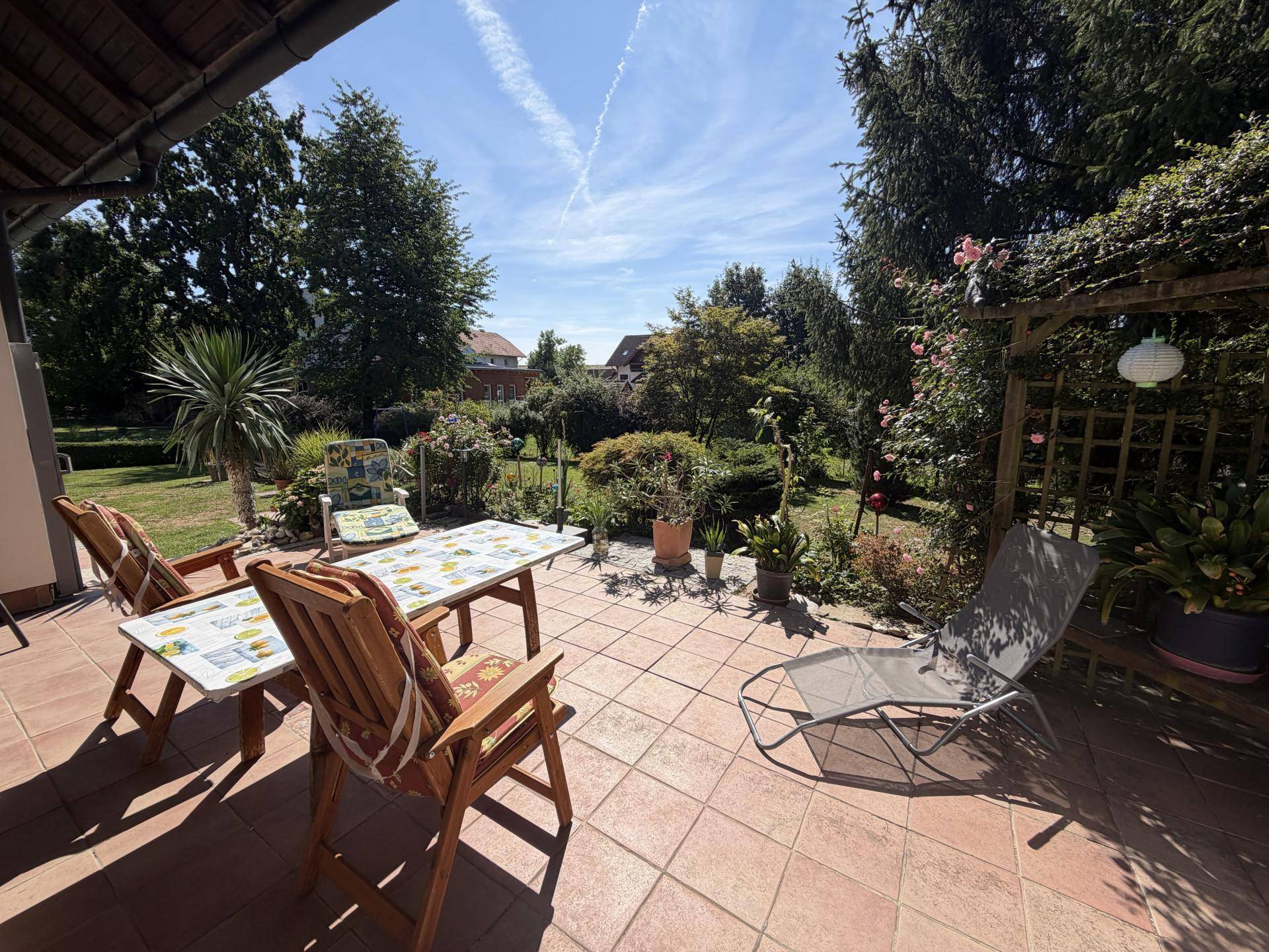 Sonnige Terrasse mit Terrakottafliesen, Gartenmöbeln und Blick ins Grüne.