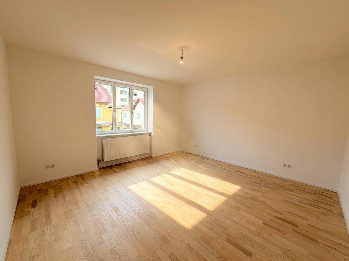 Geräumiges Zimmer mit Parkettboden, großem Fenster und sonniger Atmosphäre.