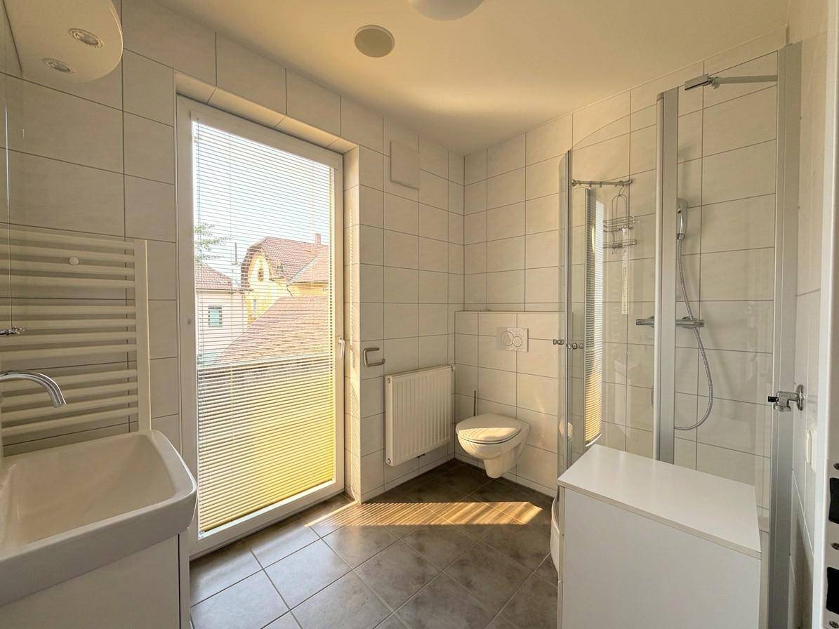 Modernes Badezimmer mit Dusche, Fenster und weiß gefliesten Wänden.