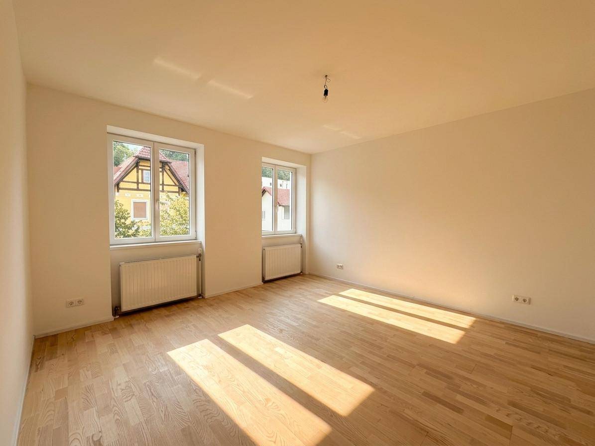 Helles Schlafzimmer mit Parkettboden, zwei Fenstern und viel Tageslicht.