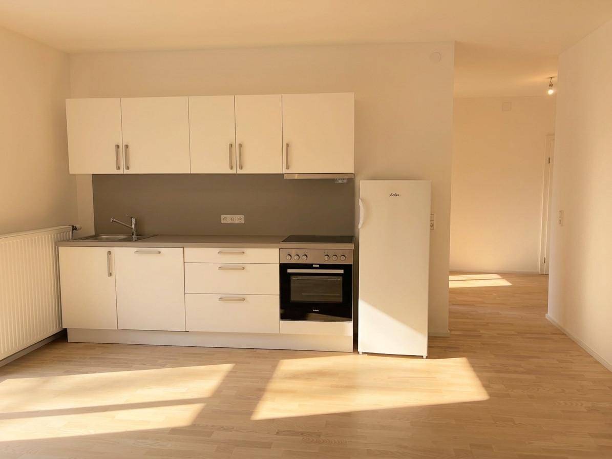 Funktionale Küchenzeile mit weißen Schränken, Kühlschrank und Kochfeld in hellem Raum.