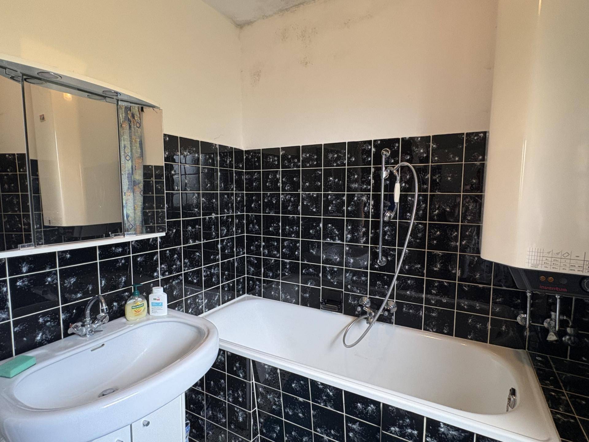Badezimmer mit schwarzen Fliesen, Badewanne und Spiegelschrank in älterem Zustand.