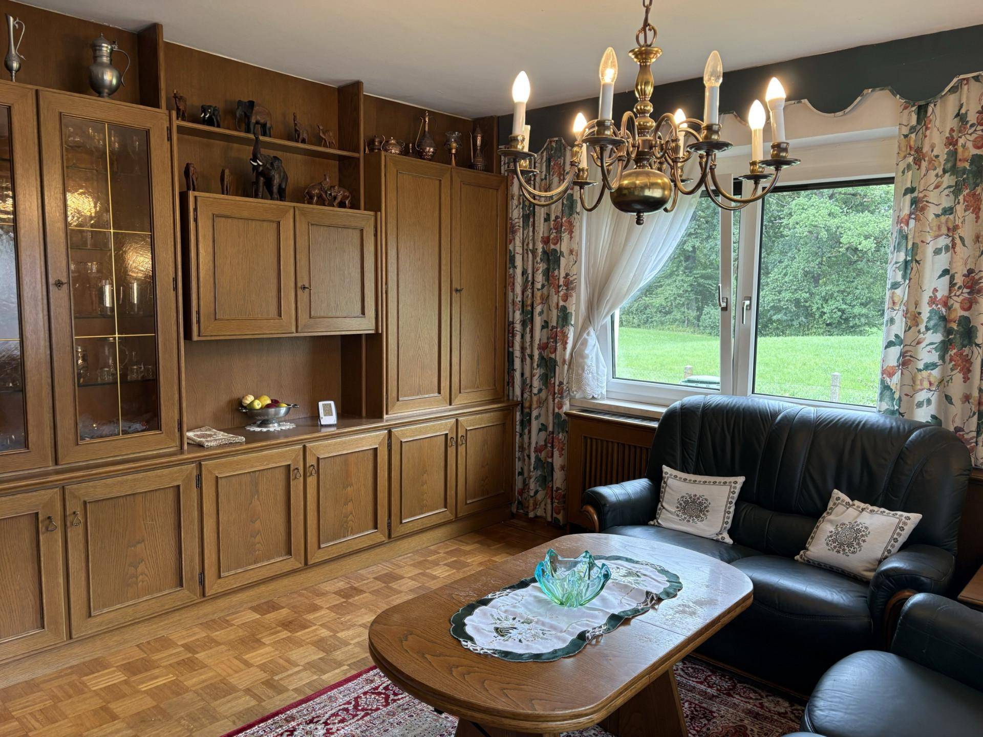 Gemütliches Wohnzimmer mit Holzmöbeln, Ledersofa und Blick ins Grüne.