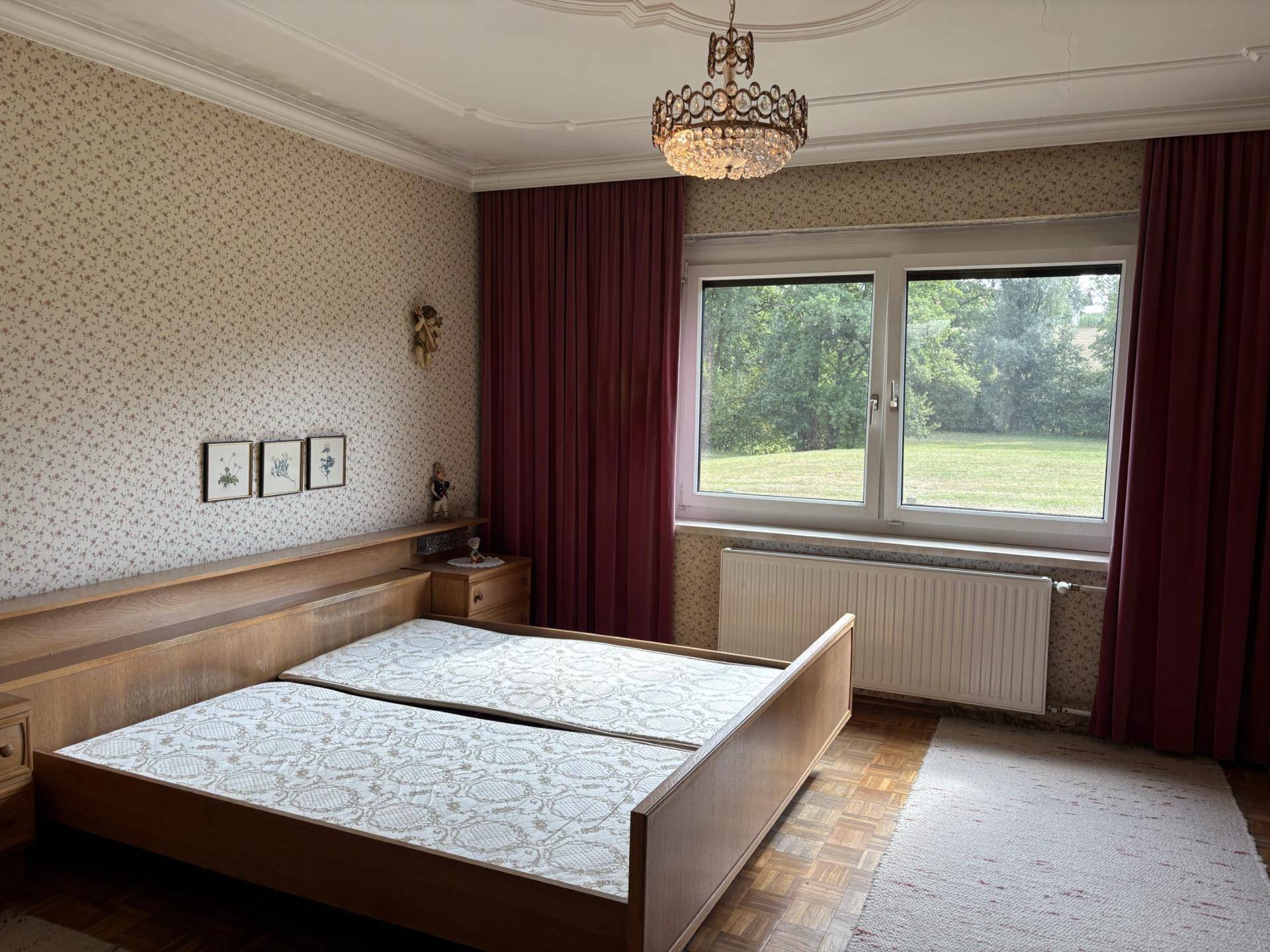 Schlafzimmer mit Doppelbett, gemusterter Tapete und weitem Blick ins Grüne.