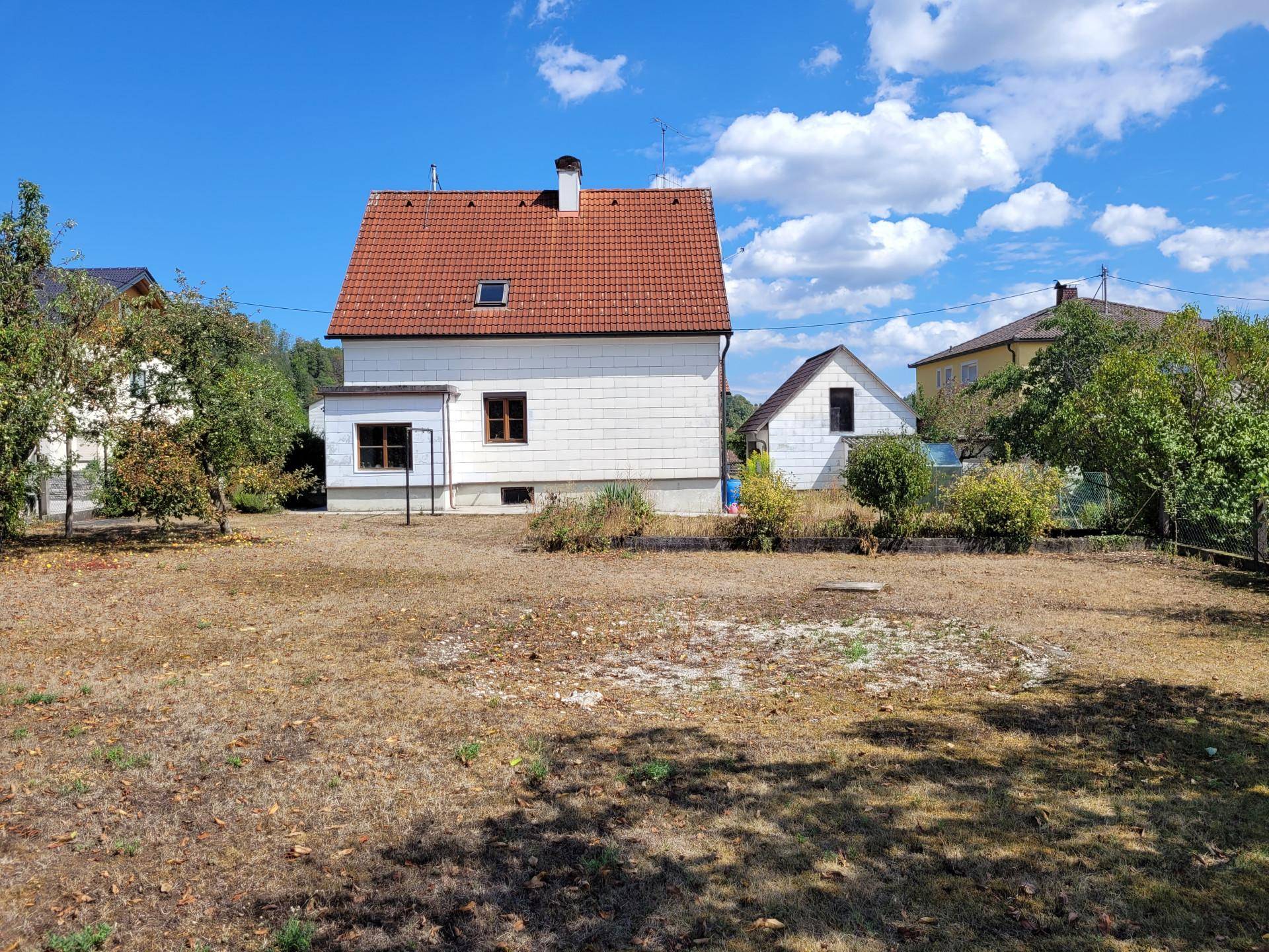 Rückansicht eines Einfamilienhauses mit großem, ungenutztem Gartenbereich unter blauem Himmel.
