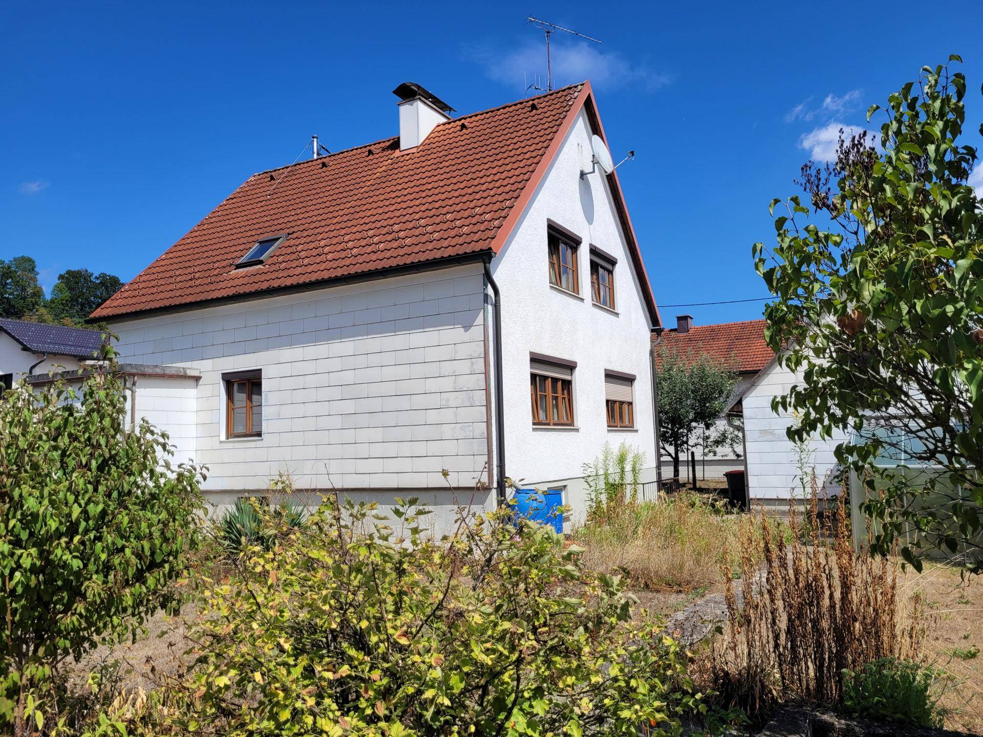 Seitenansicht des Einfamilienhauses mit rotem Dach und umliegender Natur unter strahlendem Himmel.