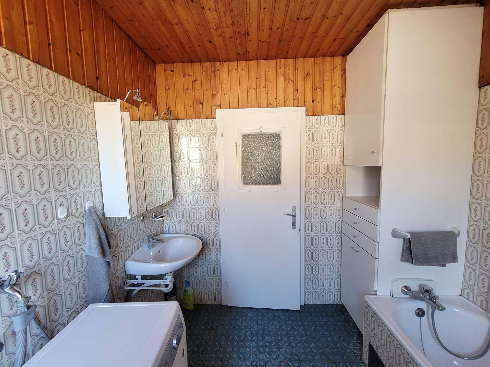 Badezimmer mit Badewanne, Waschbecken, Holzdecke und gemusterten Wandfliesen.
