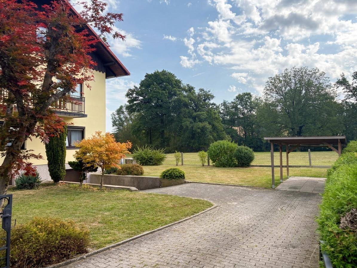 Gepflasterte Einfahrt mit Carport und weitläufigem Rasenbereich vor dem Haus.