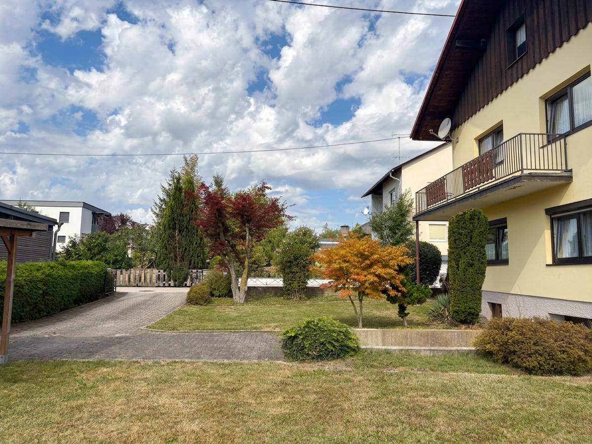 Seitenansicht des Hauses mit Balkon, gepflegtem Garten und weitläufiger Rasenfläche.