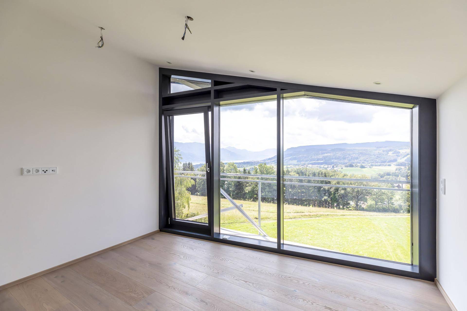 Heller Raum mit großen Fenstern und Zugang zu einem Balkon, bietet einen weiten Blick ins Grüne.