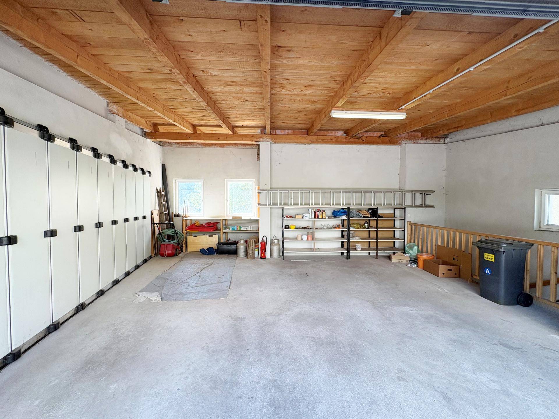 Innenansicht der großen Garage mit viel Stauraum, Regalen und Holzdecke.
