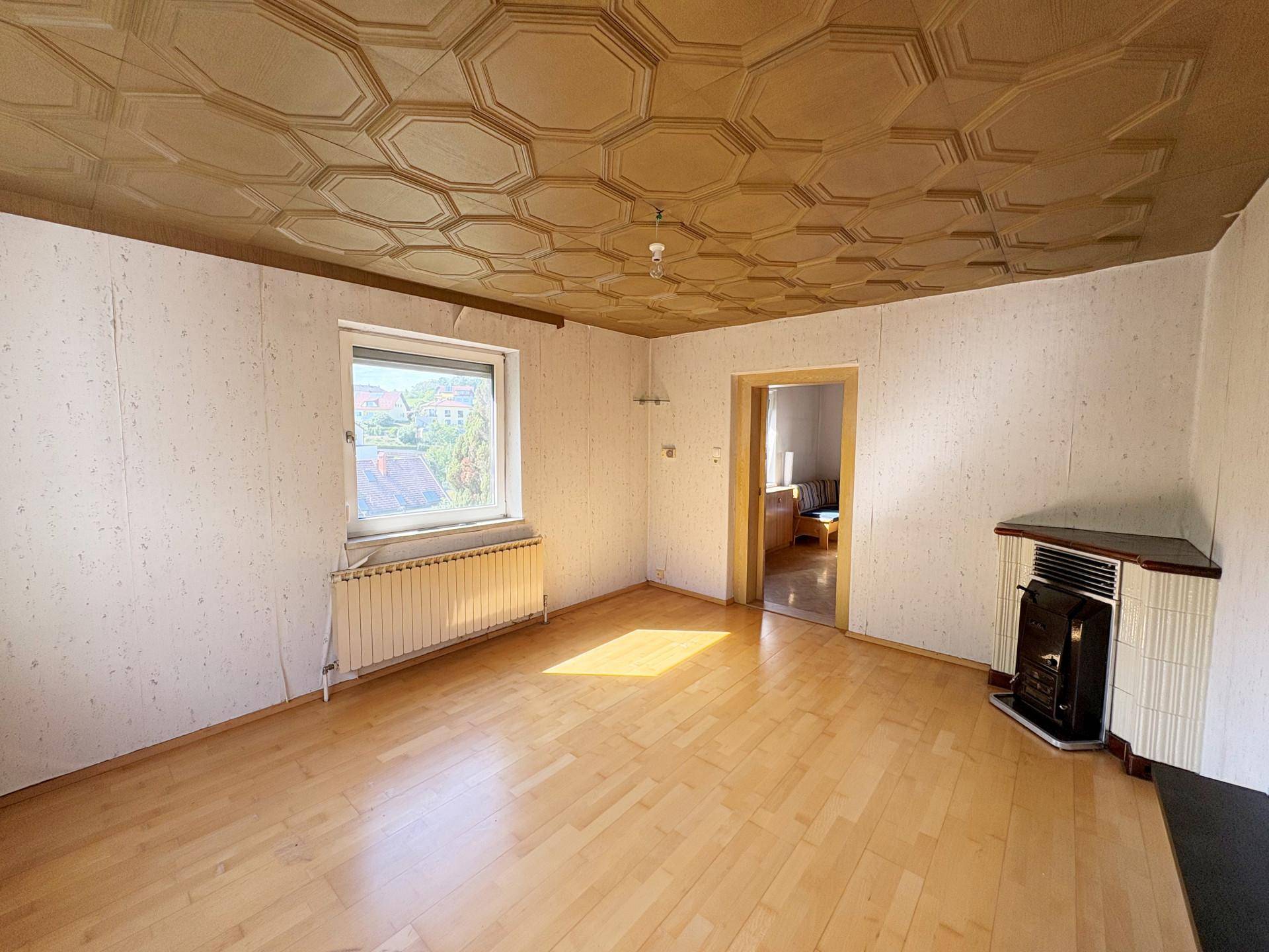 Wohnzimmer mit Parkettboden, Kachelofen und dekorativer Deckenverkleidung.
