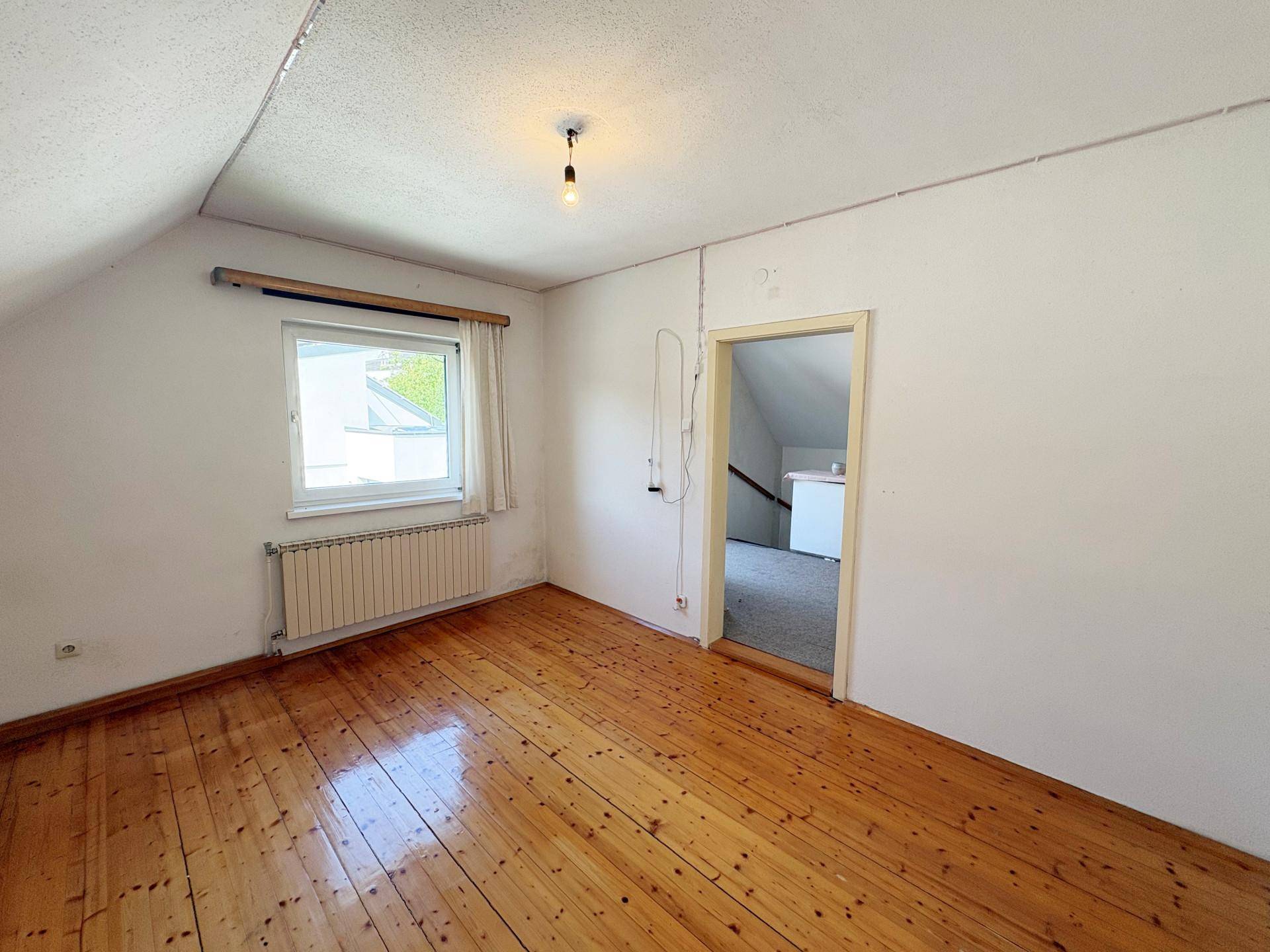 Schlafzimmer im Dachgeschoss mit Holzdielenboden und schrägen Wänden.