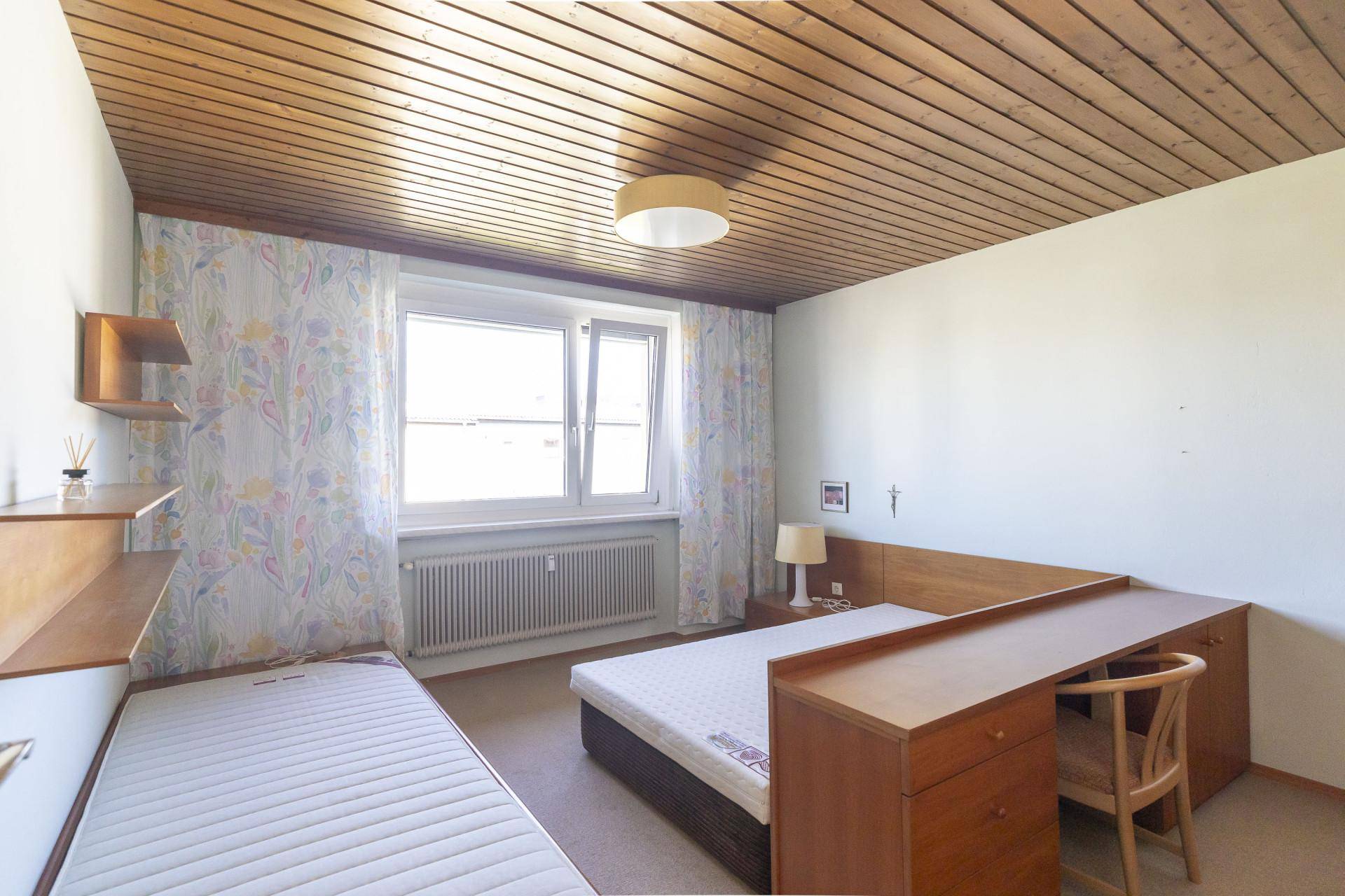 Schlafzimmer mit zwei Betten, Holzdecke und großem Fenster für viel Tageslicht.