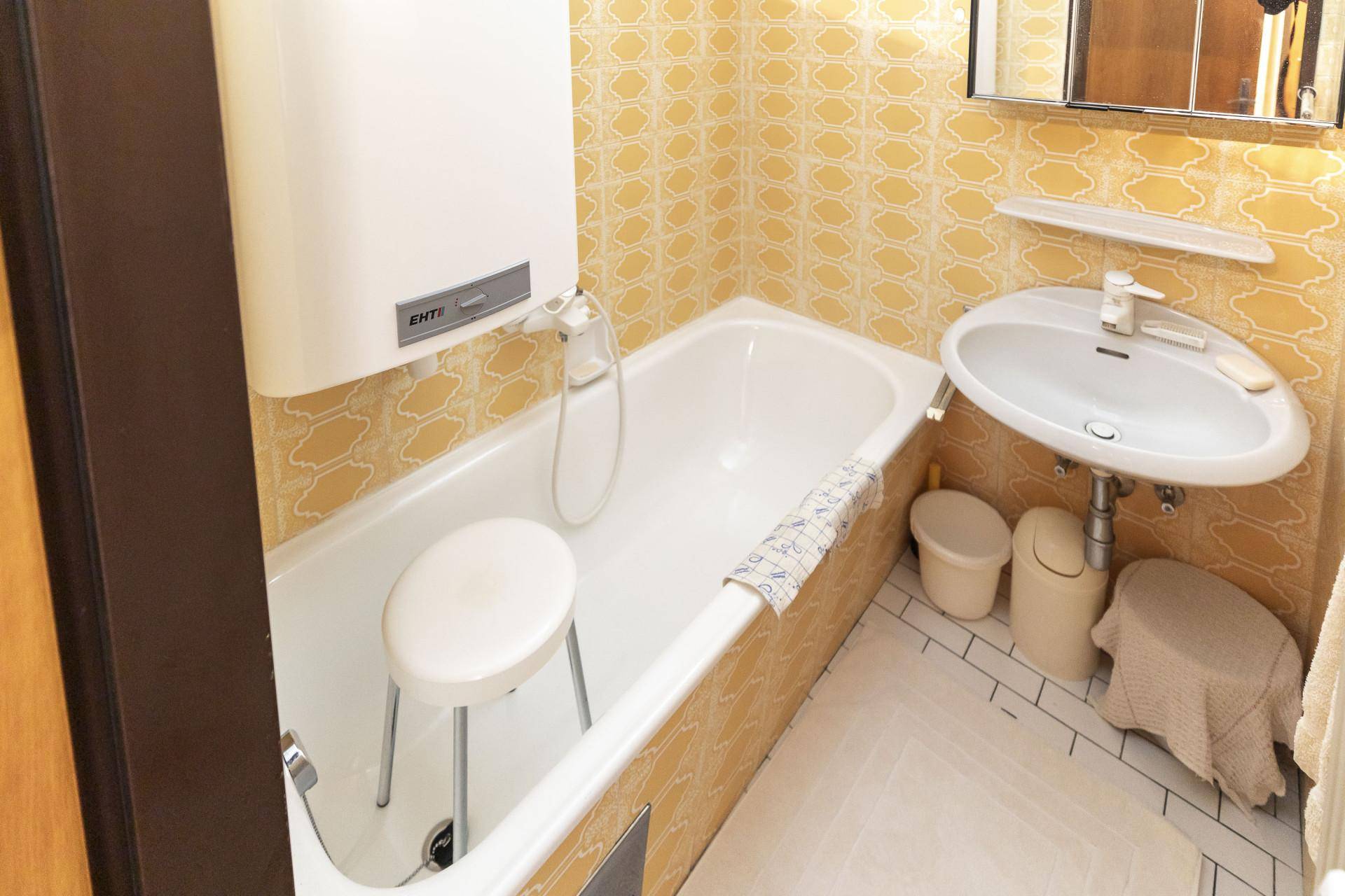 Kleines Badezimmer mit Badewanne, Waschbecken und gelben Retro-Fliesen an den Wänden.
