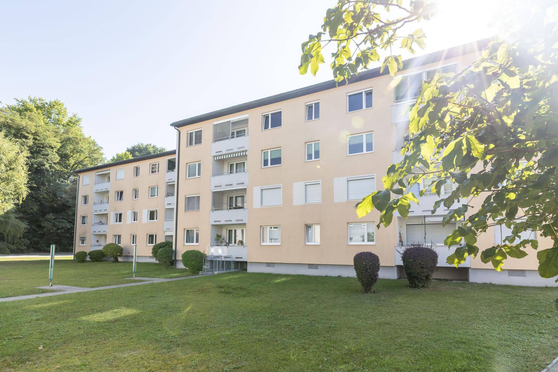 Wohngebäude mit Balkonen und grüner Umgebung unter strahlendem Sonnenschein.