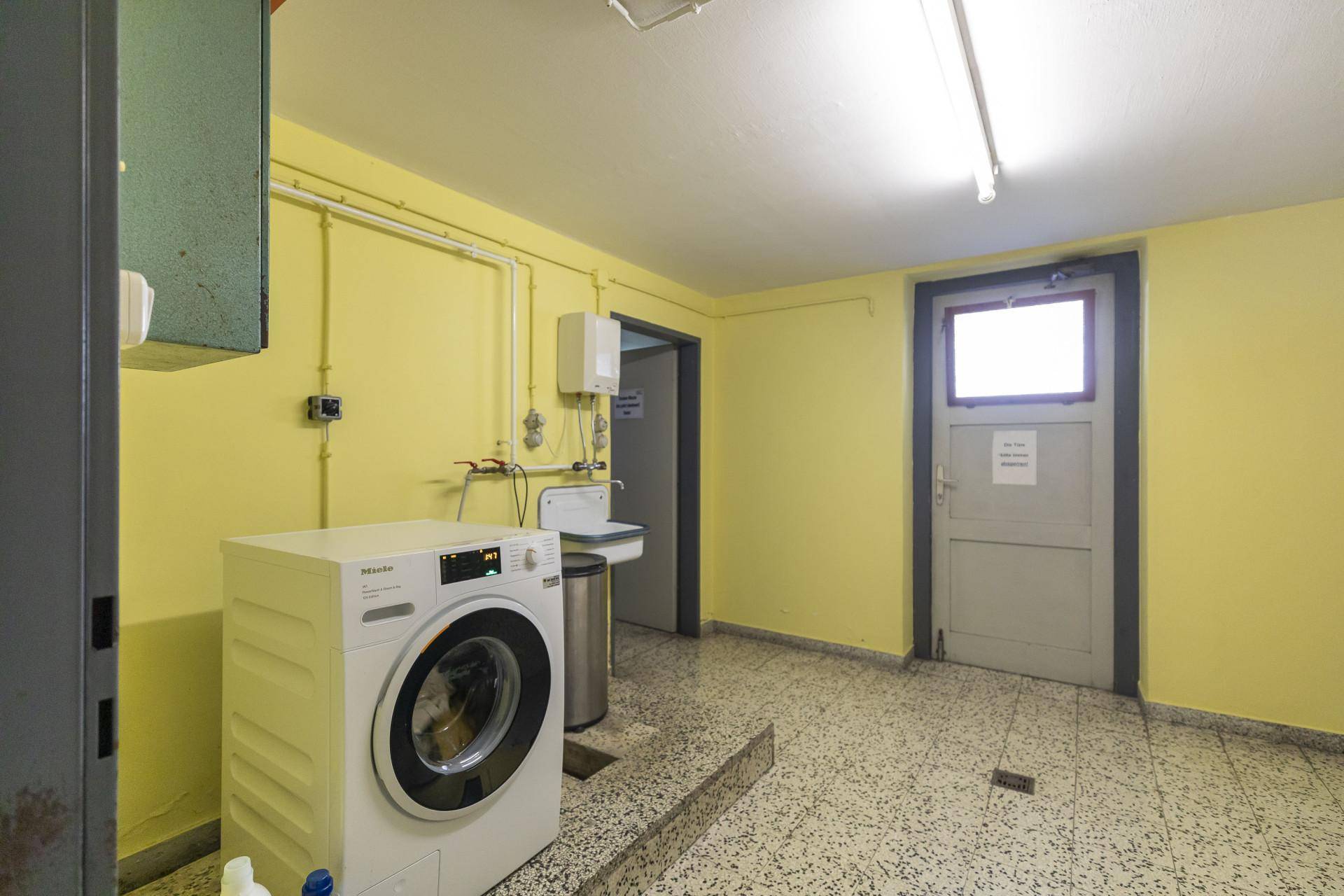 Gemeinschaftlicher Waschraum im Keller mit Waschmaschine und Waschbecken.