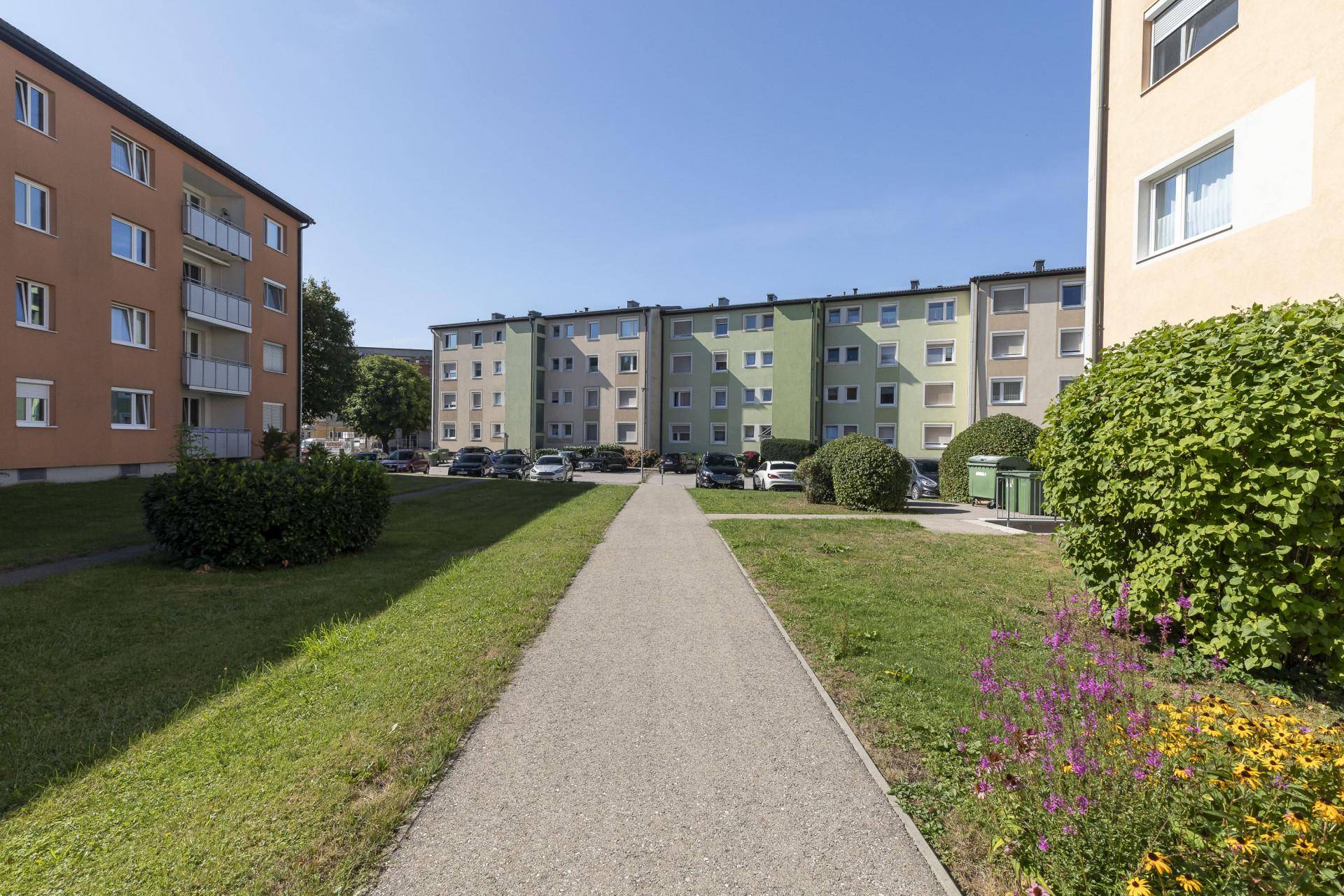 Wohnanlage mit mehreren Gebäuden, Grünflächen und Parkplätzen an einem sonnigen Tag.