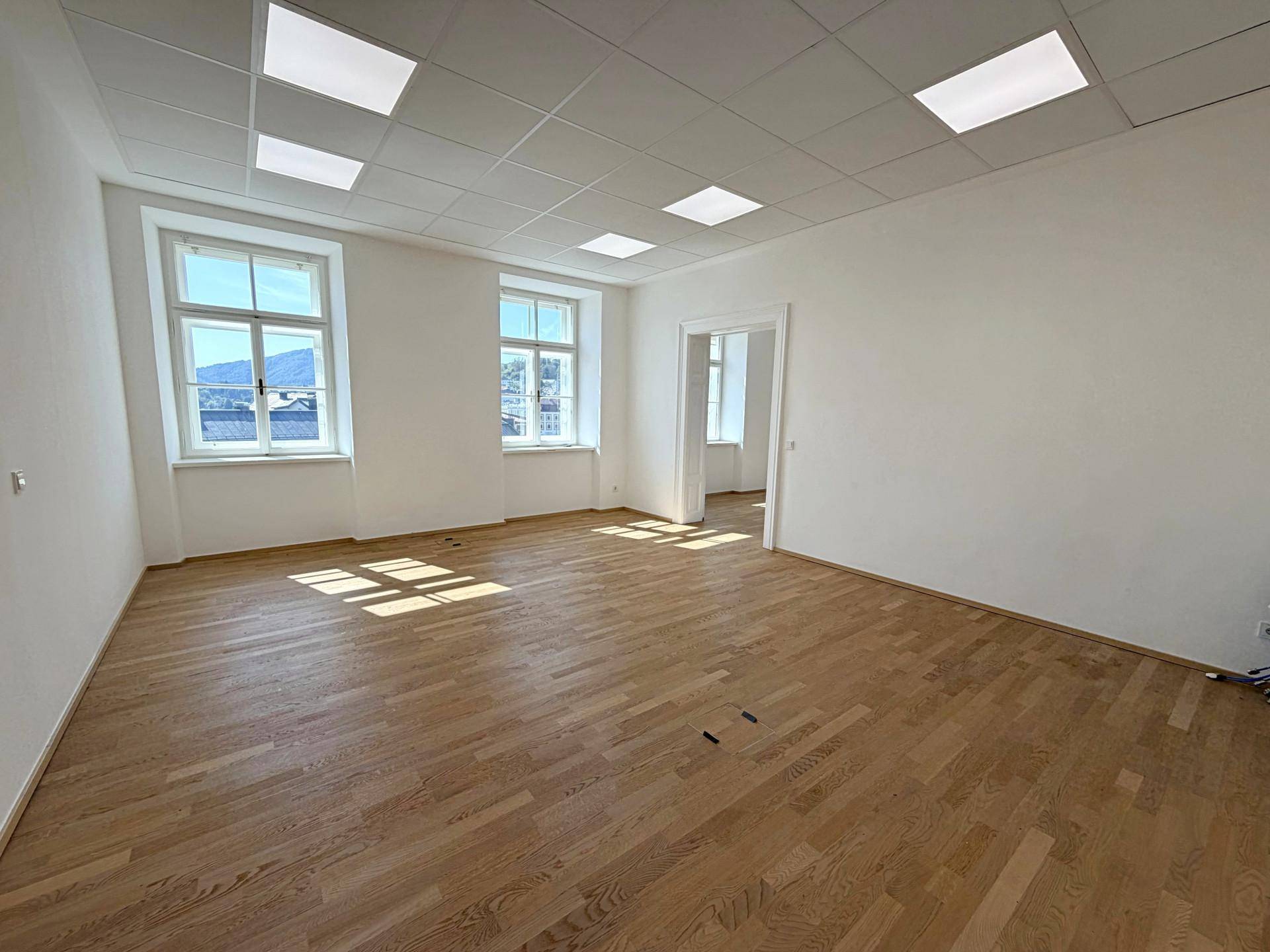 Großer, heller Raum mit Holzboden und Fenstern, die einen weiten Blick nach draußen ermöglichen.
