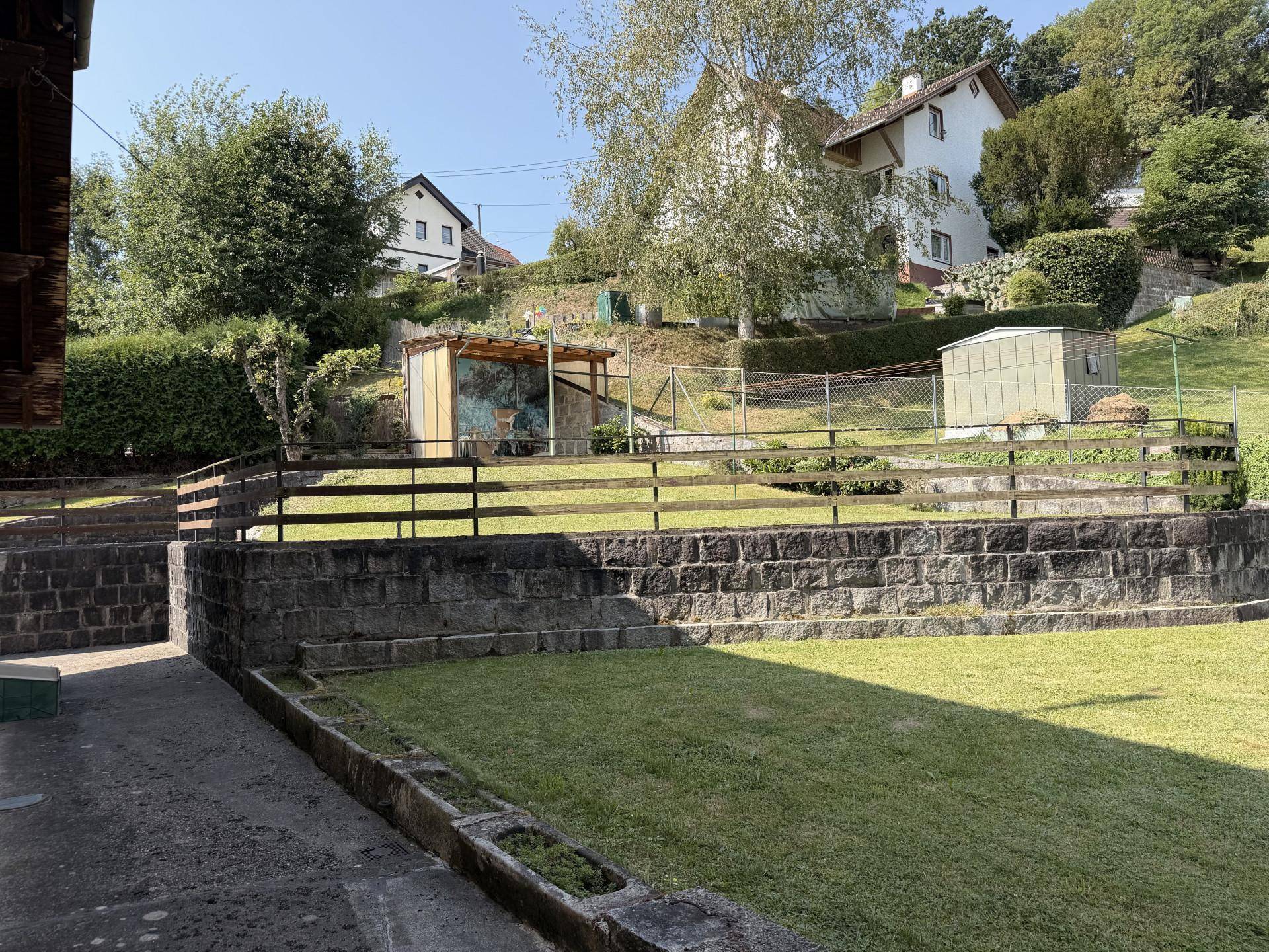 Gestufter Gartenbereich mit Rasenflächen und Steinmauern, umgeben von weiteren Wohnhäusern.