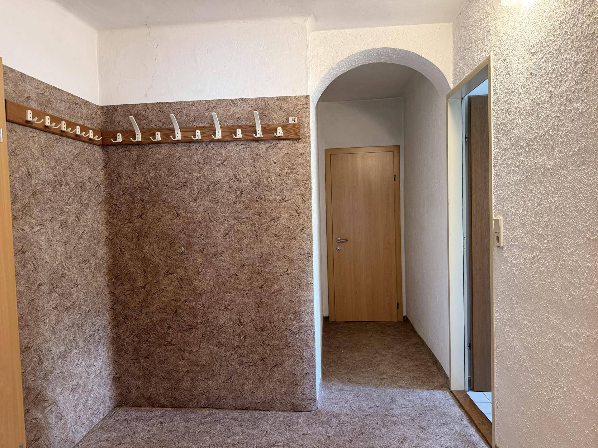 Eingangsbereich mit Garderobe und gemusterter Tapete, der zu weiteren Räumen führt.