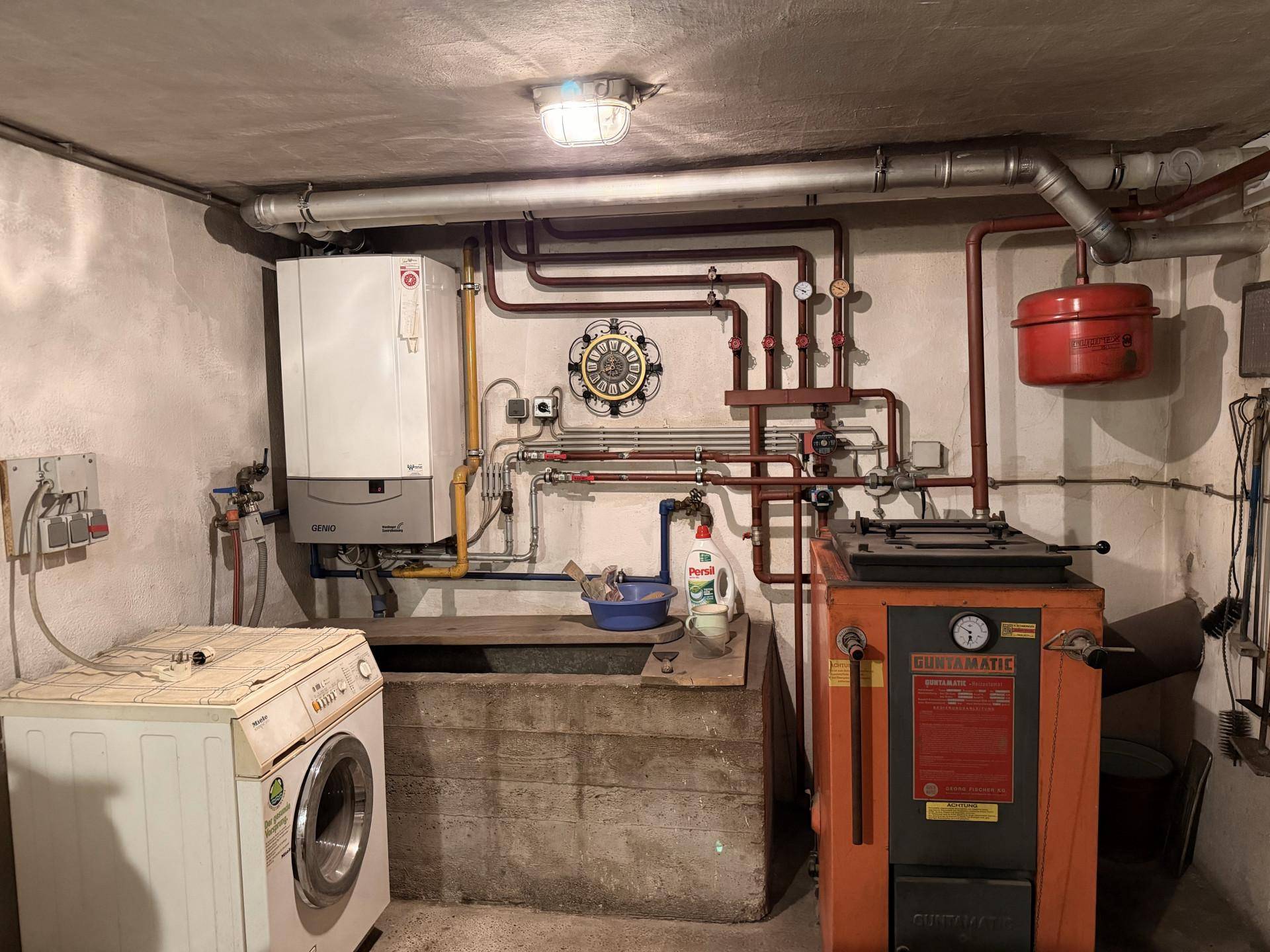 Heizungsraum im Keller mit Gastherme, Warmwasserspeicher und Waschmaschine, funktional eingerichtet.