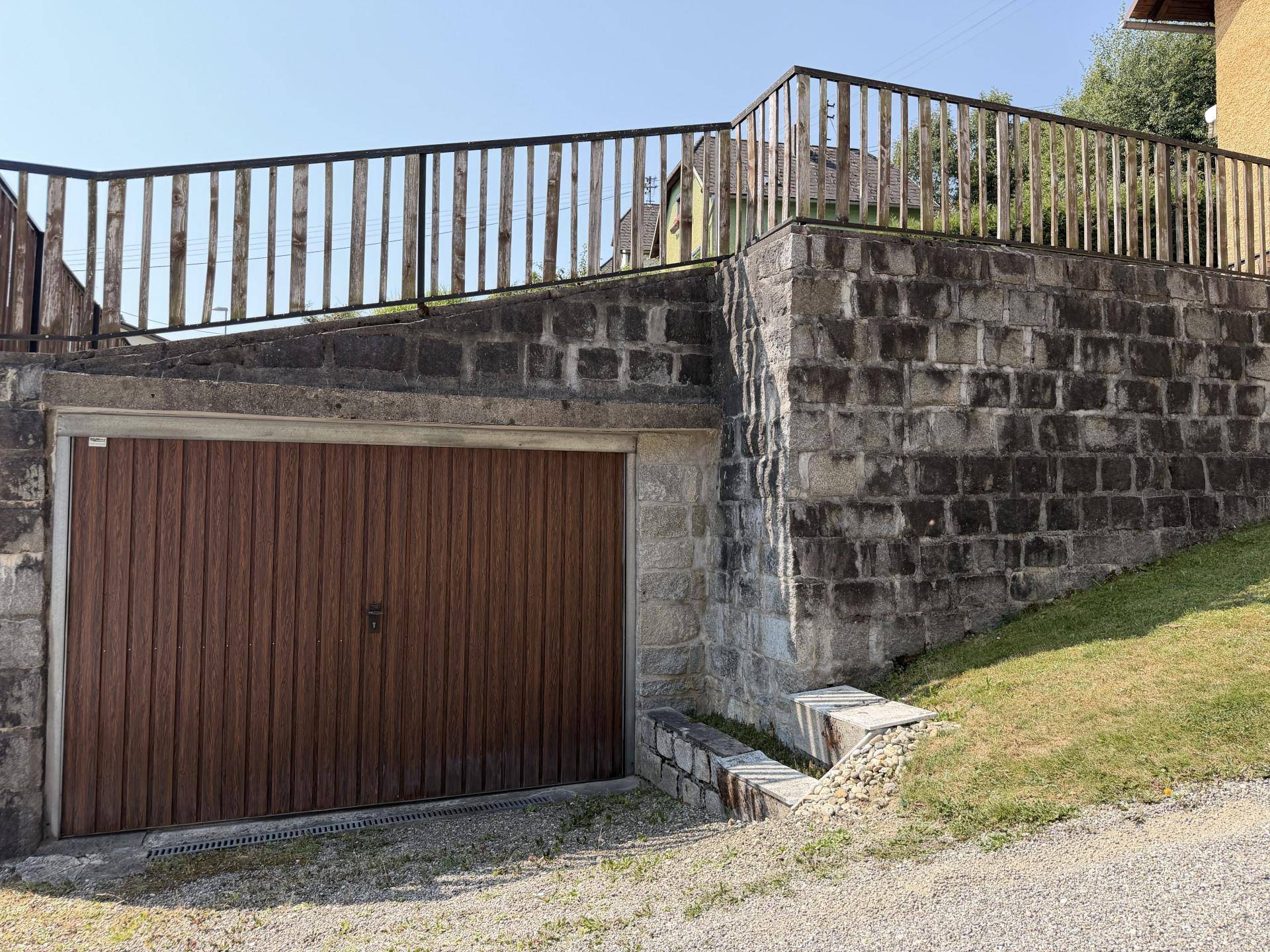 Garage mit Holztor, eingebettet in eine robuste Steinmauer, bietet sicheren Stellplatz.