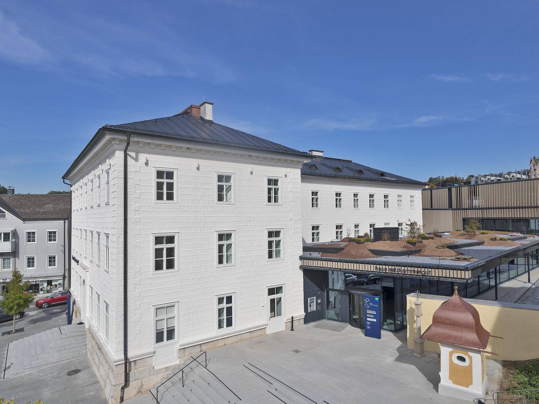 Eindrucksvolles weißes Gebäude mit klassischer Architektur und modernem Eingangsbereich unter blauem Himmel.