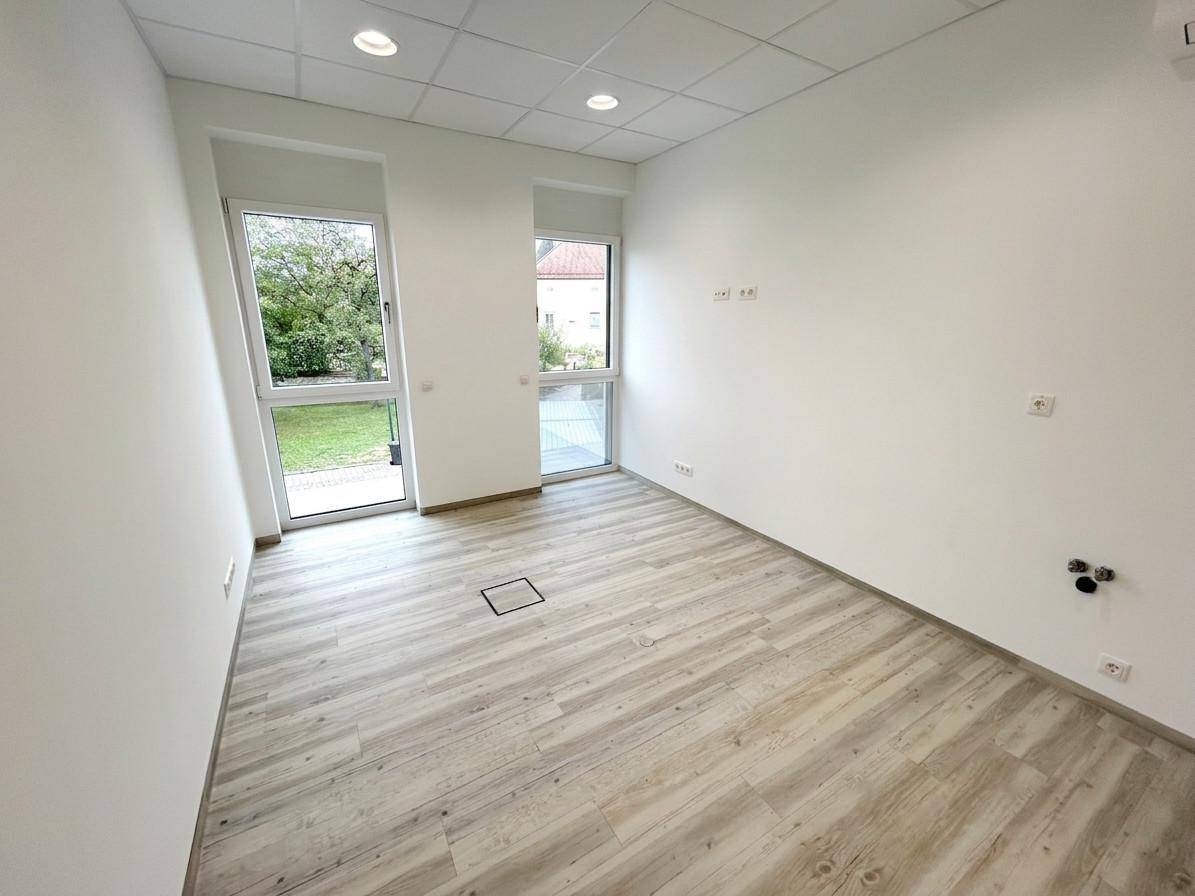 Heller Raum mit Anschlüssen für eine Küche und Blick ins Grüne durch die Fenster.