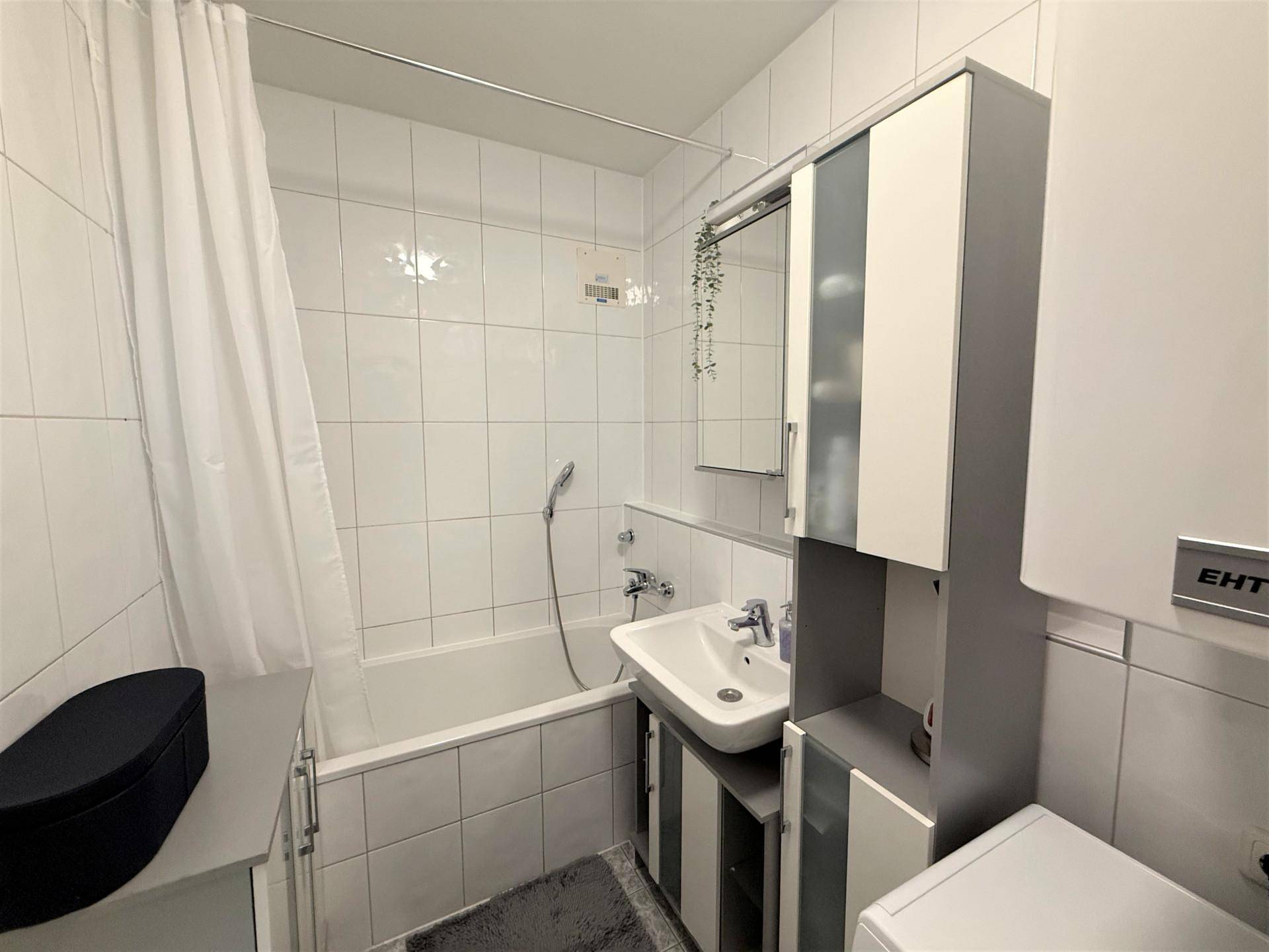 Badezimmer mit Badewanne, Duschvorhang, Waschbecken und weißen Fliesen, funktional und hell.