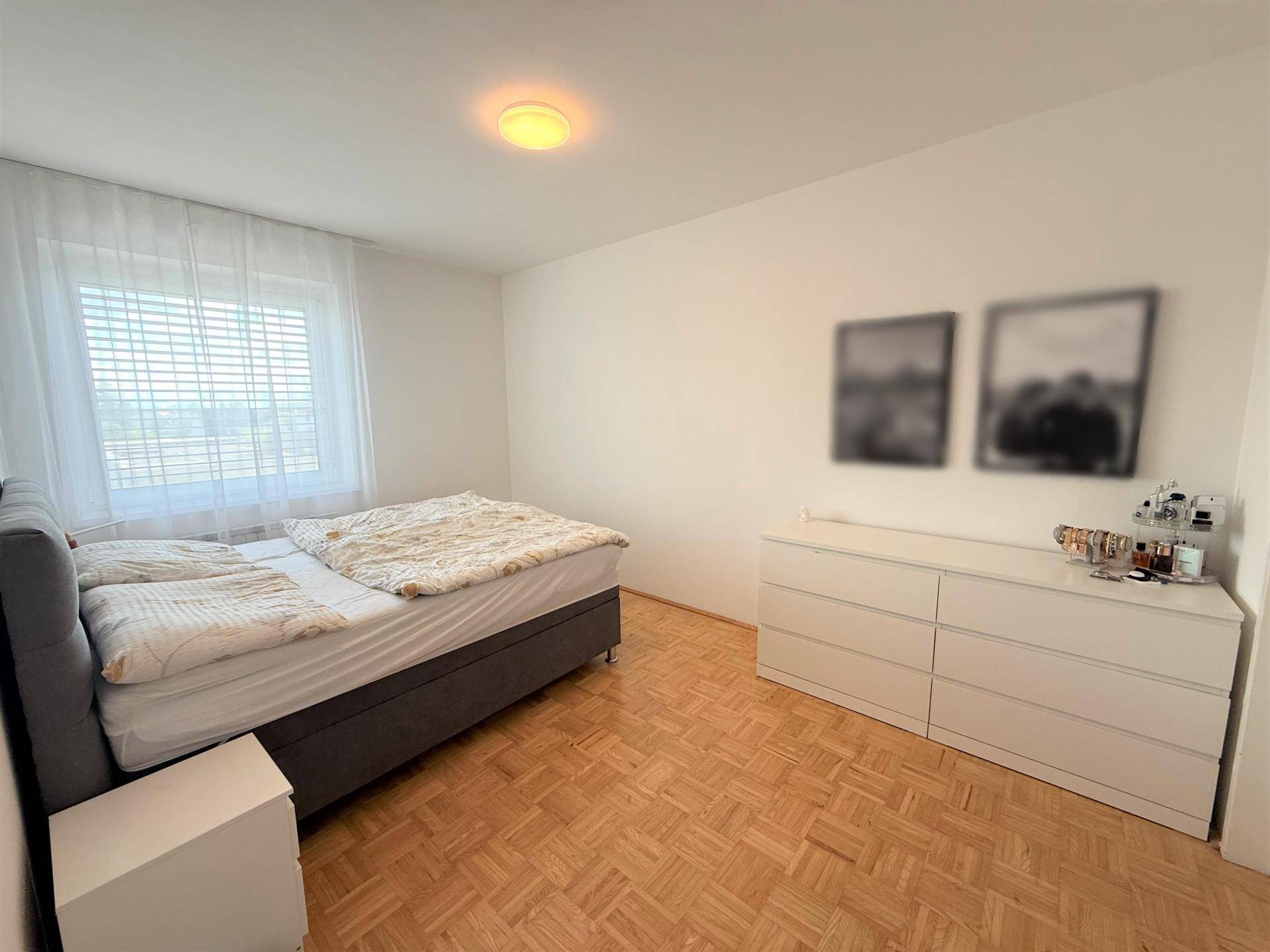 Helles Schlafzimmer mit Doppelbett, Kommode und Parkettboden, sorgt für eine gemütliche Atmosphäre.