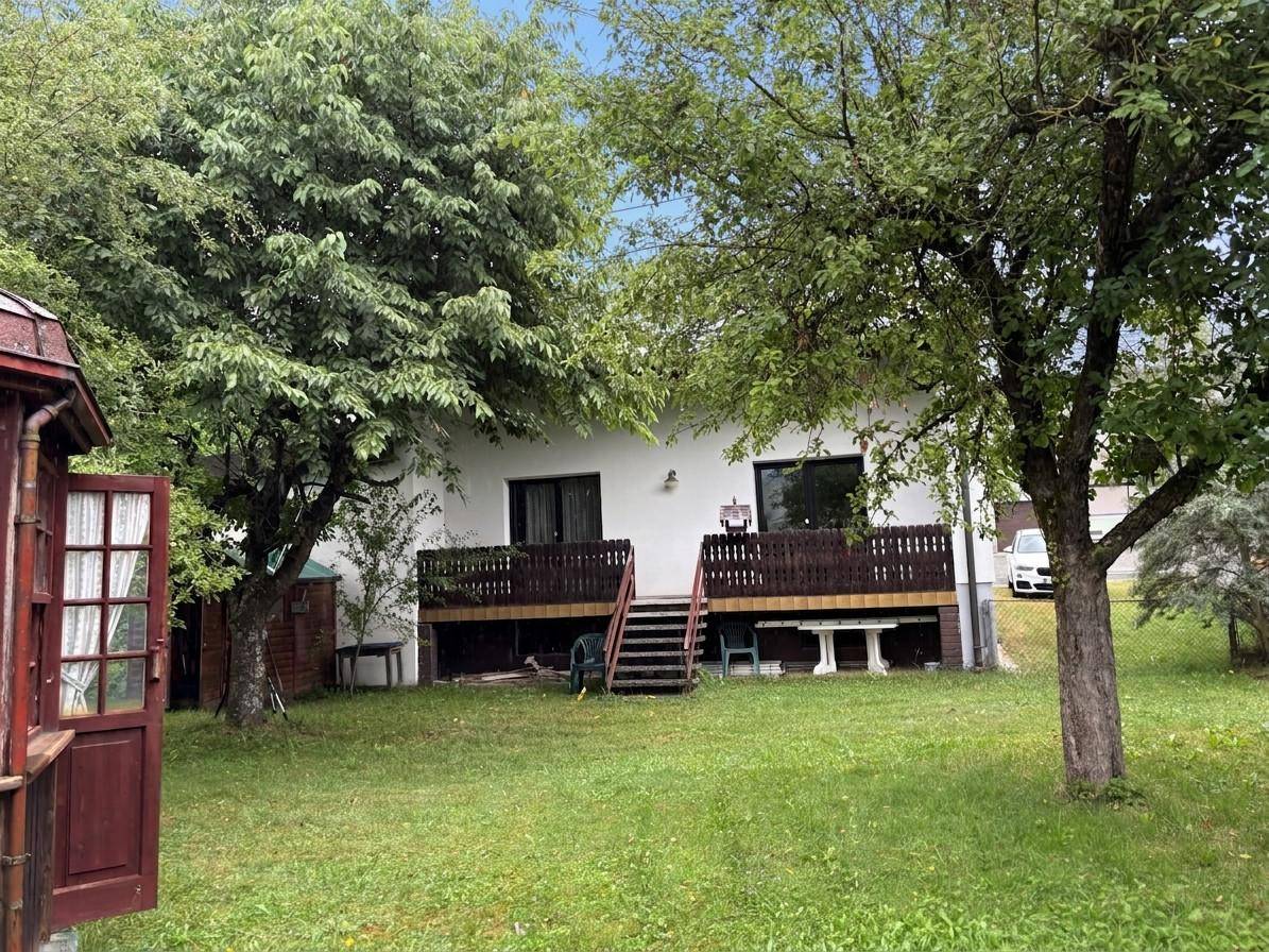 Gepflegter Garten hinter dem Haus mit Rasenfläche, Bäumen und Holzterrasse.