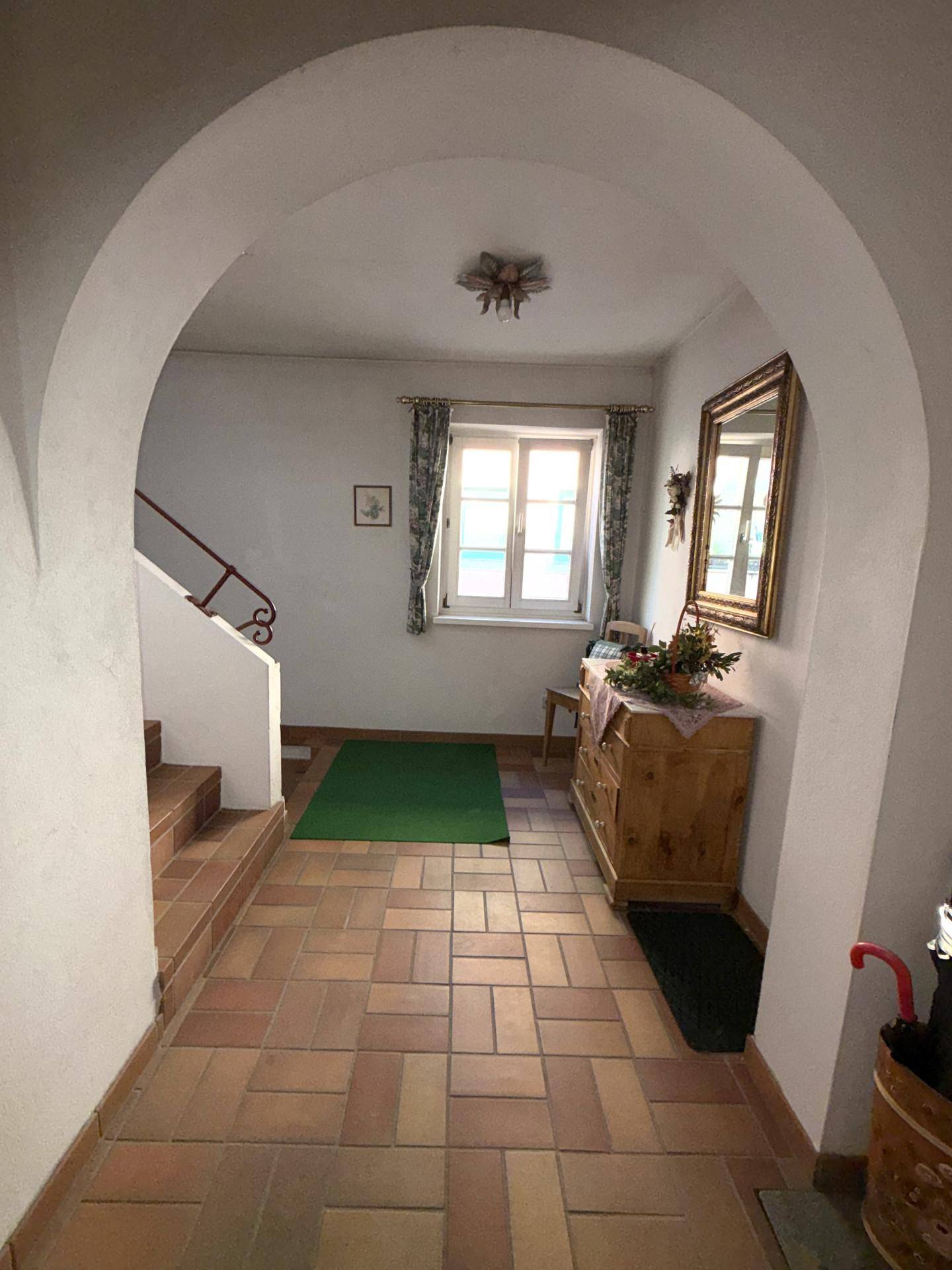Heller Flur mit Terrakotta-Fliesenboden, einem eleganten Bogen und einem Fenster für natürliches Licht.