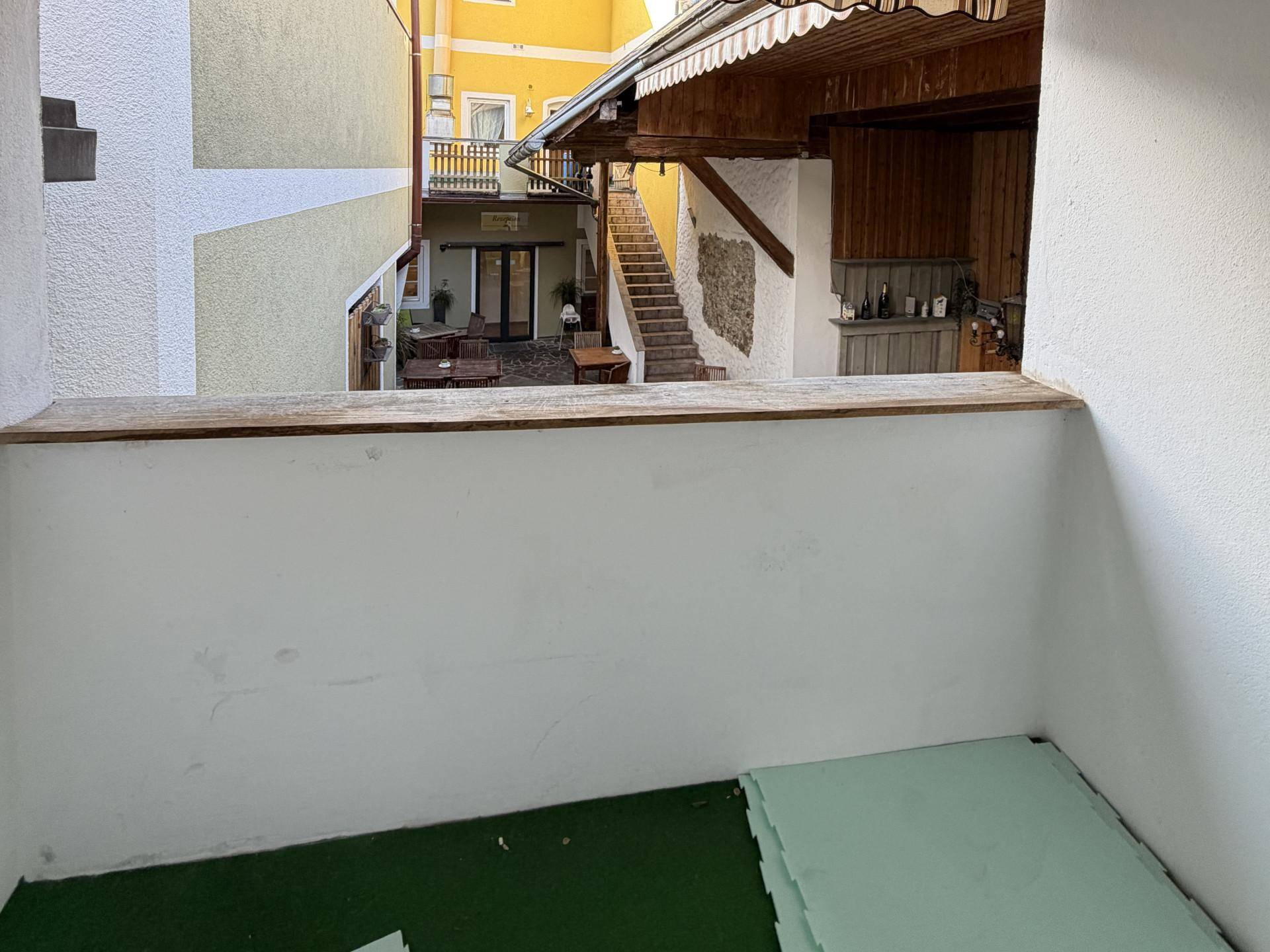 Blick von einem kleinen Balkon in einen Innenhof mit Außensitzbereich und Treppenaufgang.