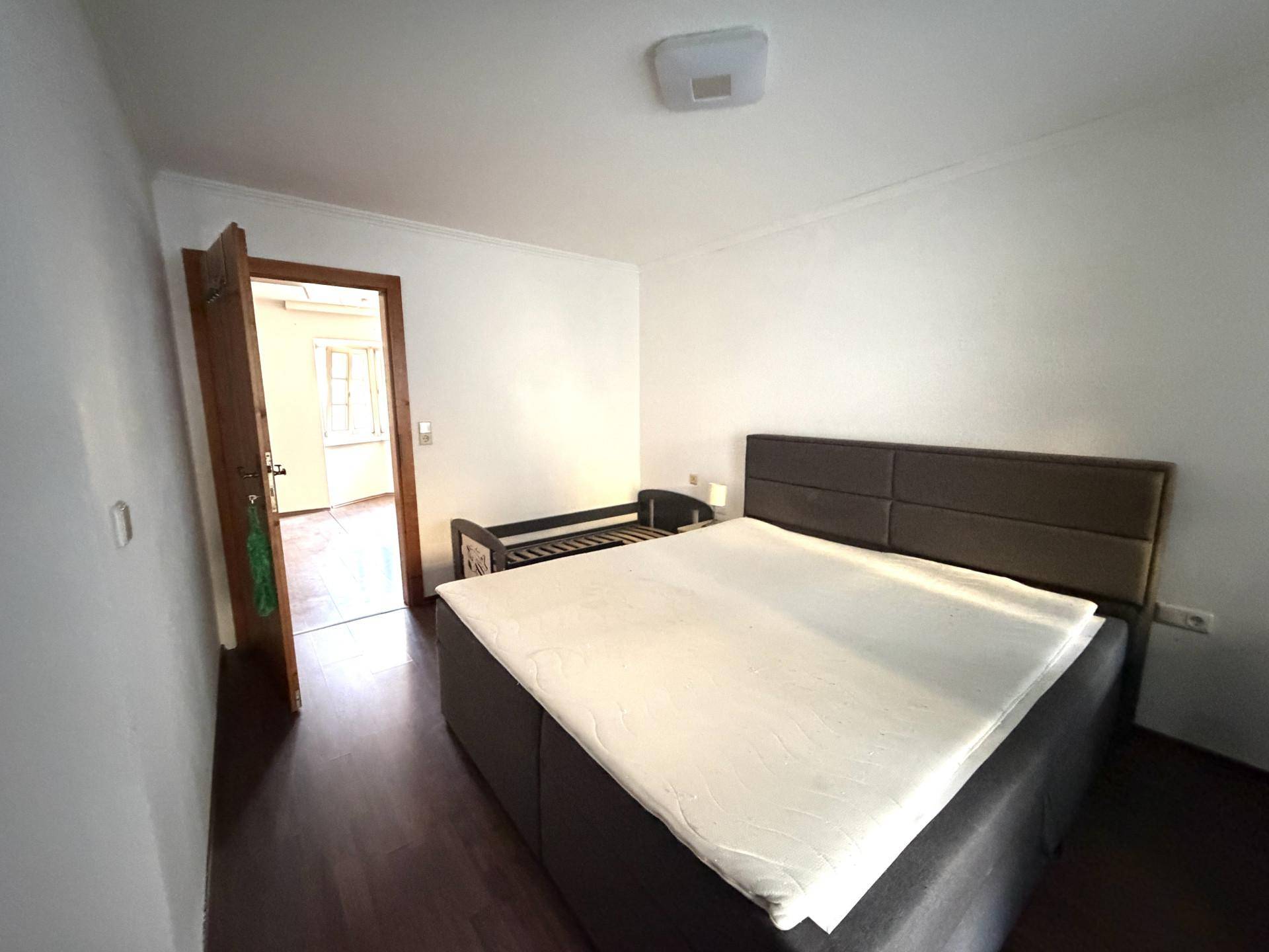 Schlafzimmer mit großem Bett und dunklem Laminatboden, bietet direkten Zugang zu einem weiteren Raum.
