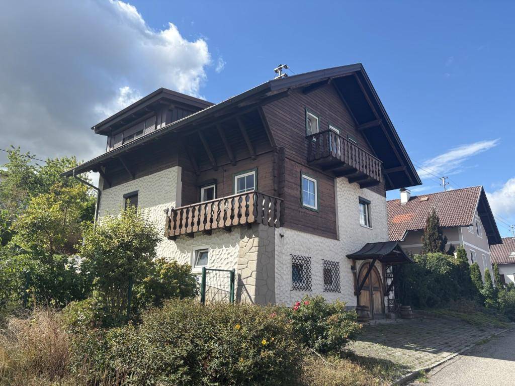 Traditionelles Haus mit Holzfassade, Steinakzenten und Balkonen unter einem Satteldach, umgeben von einem gepflegten Garten.
