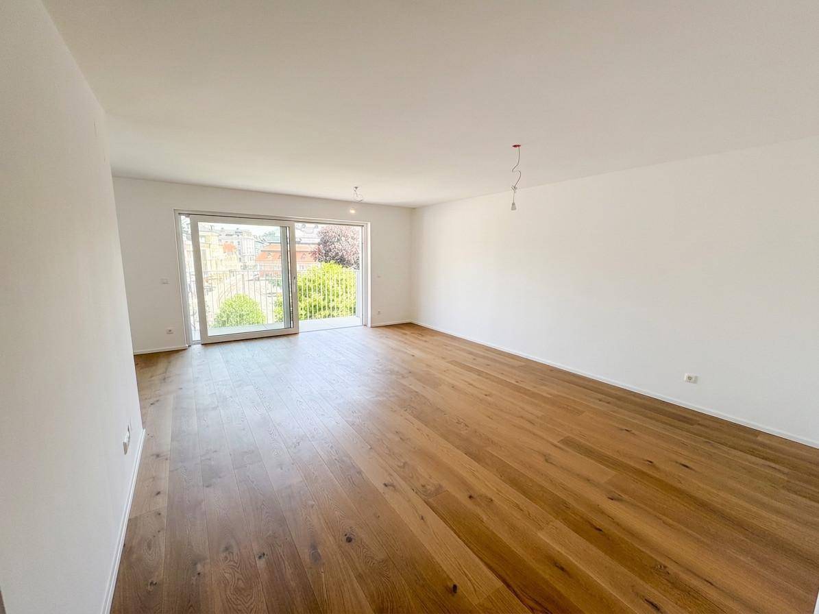 Lichtdurchfluteter Raum mit Eichenparkett und Zugang zu einem Balkon oder einer Terrasse.