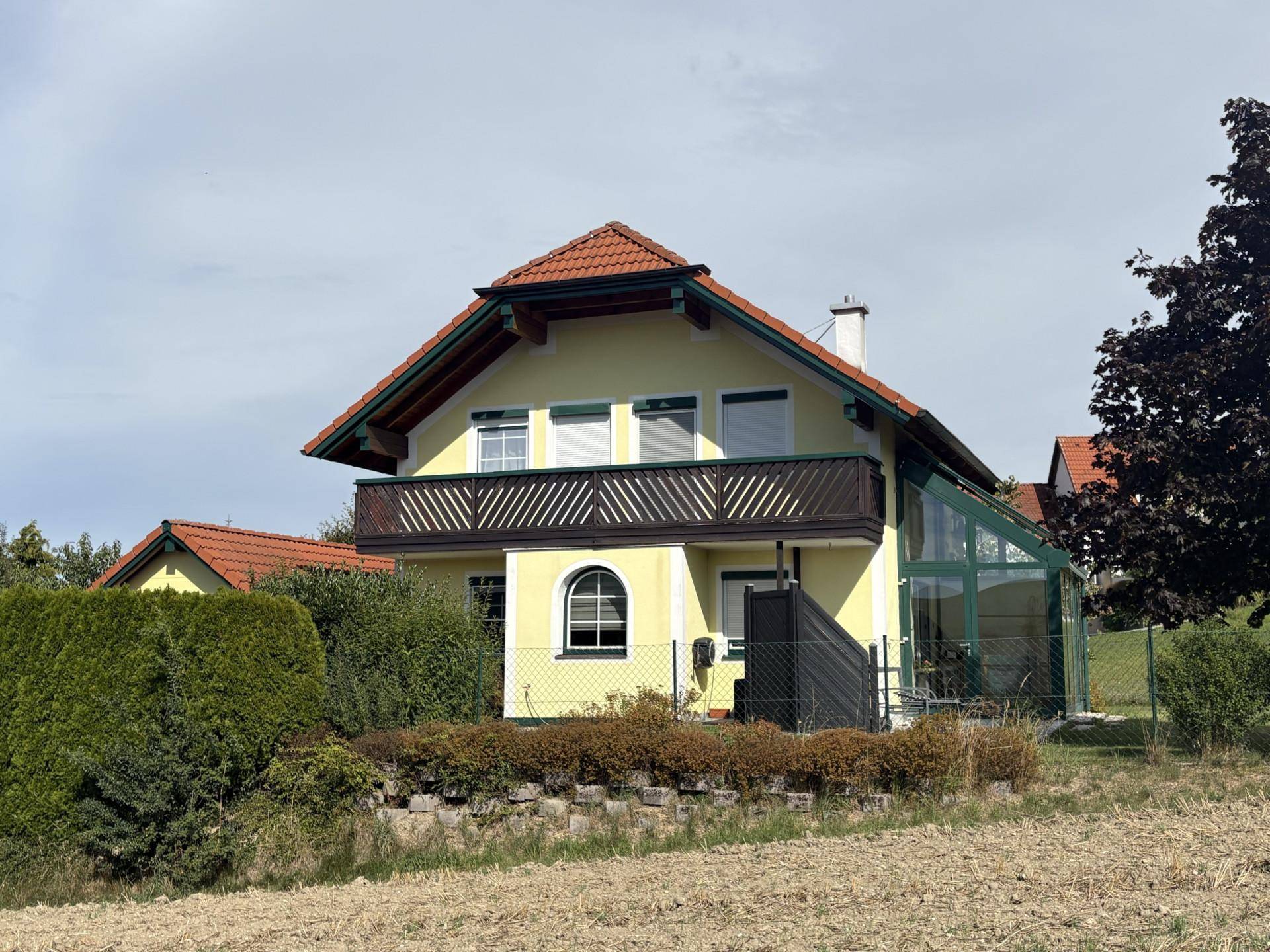 Rückansicht des Hauses mit Balkon, Wintergarten und umgebender Hecke.
