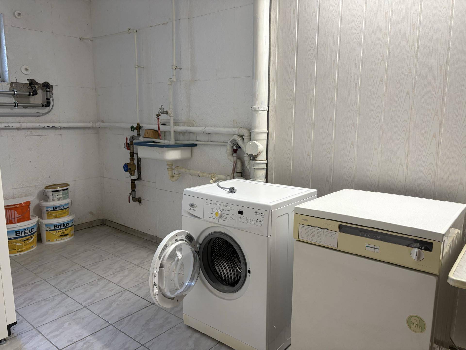 Waschküche im Keller mit Waschmaschine, Trockner und Waschbecken.
