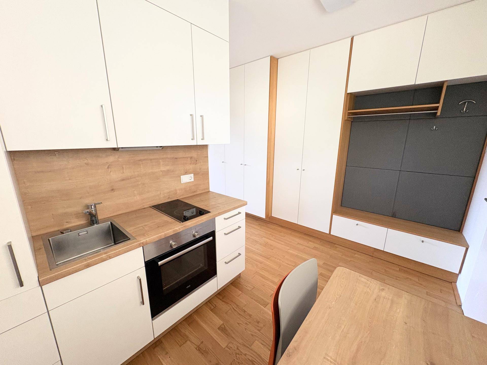 Kompakte Einbauküche mit weißen Schränken, Holz-Arbeitsplatte und integrierten Geräten.