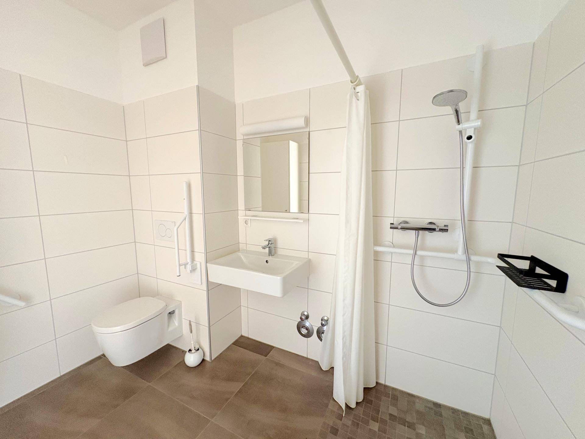 Barrierefreies Badezimmer mit ebenerdiger Dusche, Wand-WC und Haltegriffen für Komfort.
