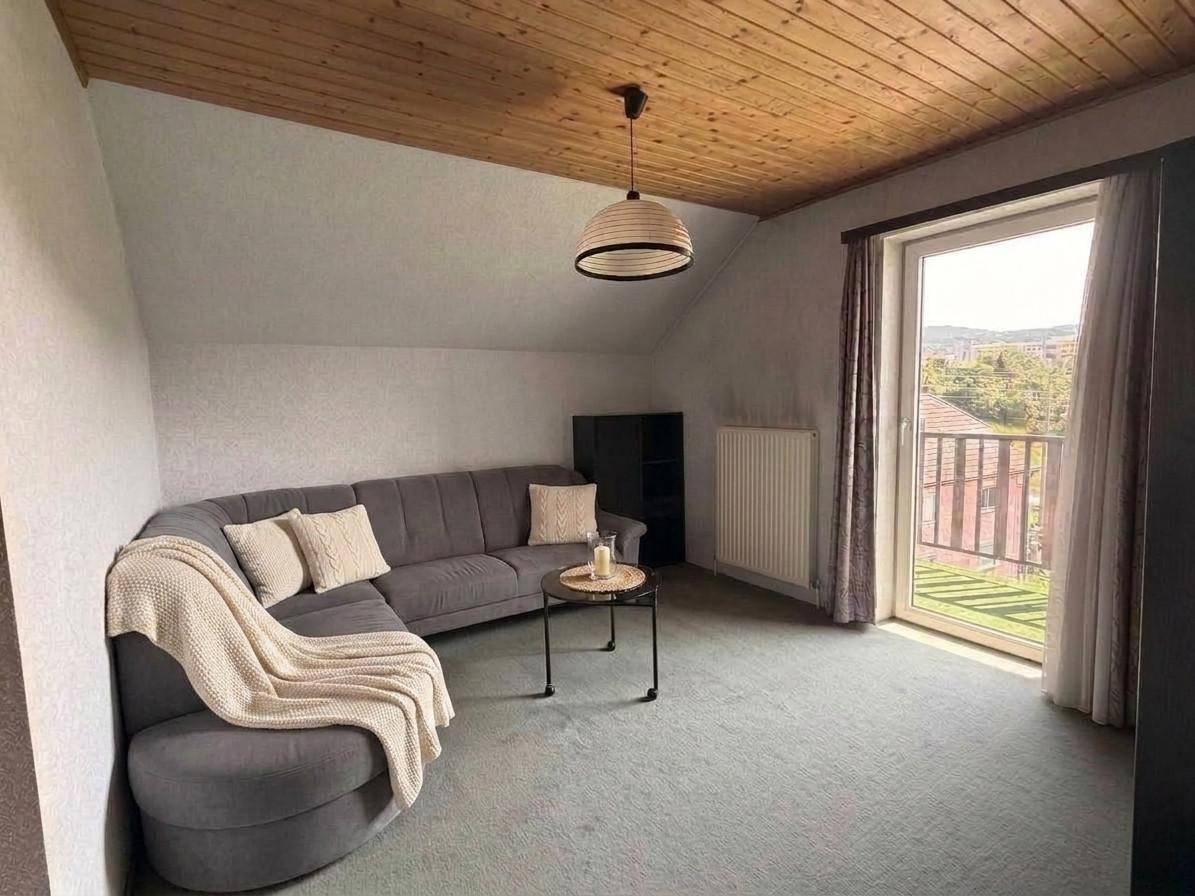 Wohnraum im Dachgeschoss mit Holzdecke, gemütlichem Ecksofa und Zugang zu einem Balkon mit Weitblick.